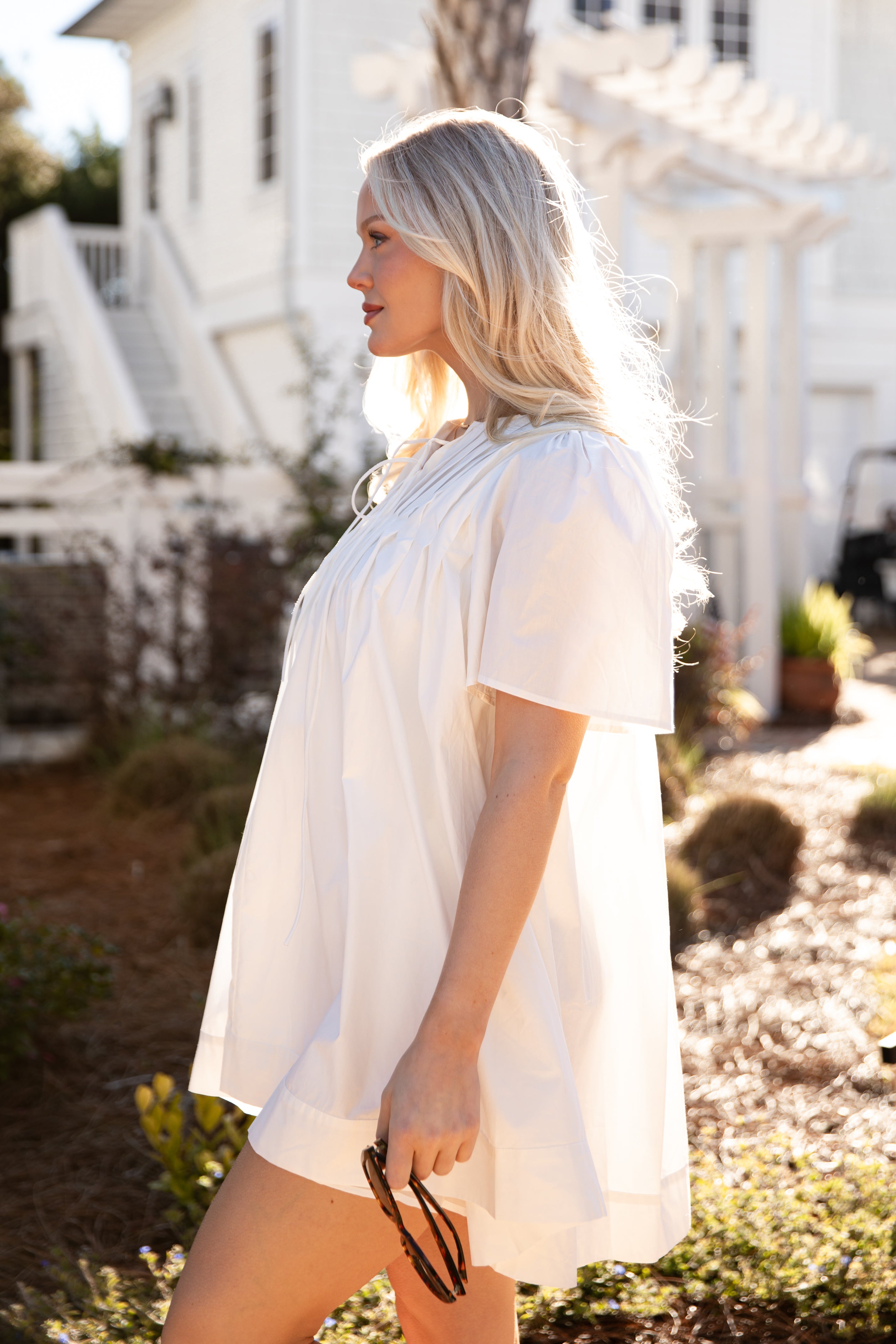 Woman wearing a white dress standing outdoors with a house in the background