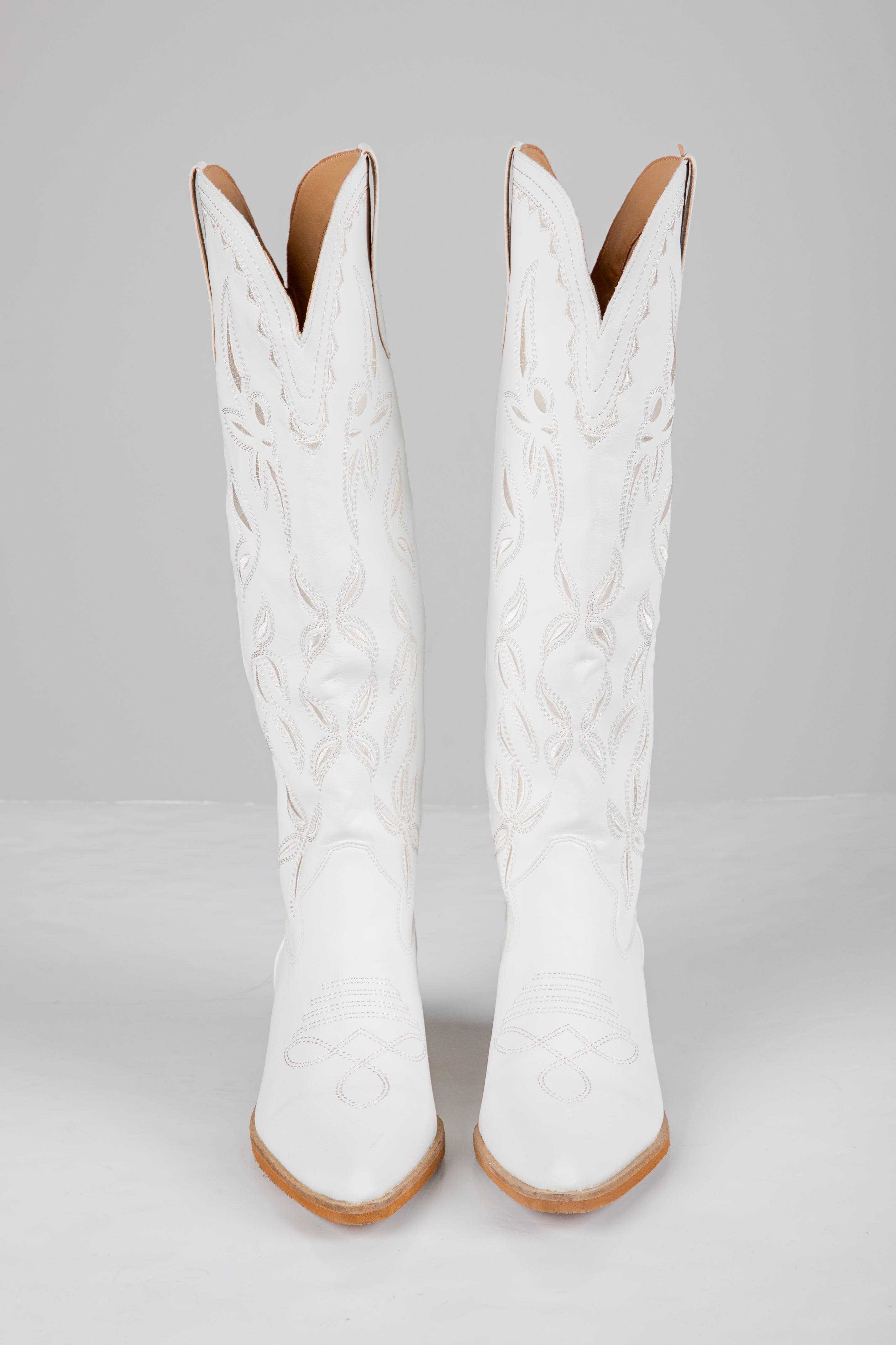 Pair of white cowboy boots with brown soles on a light gray background