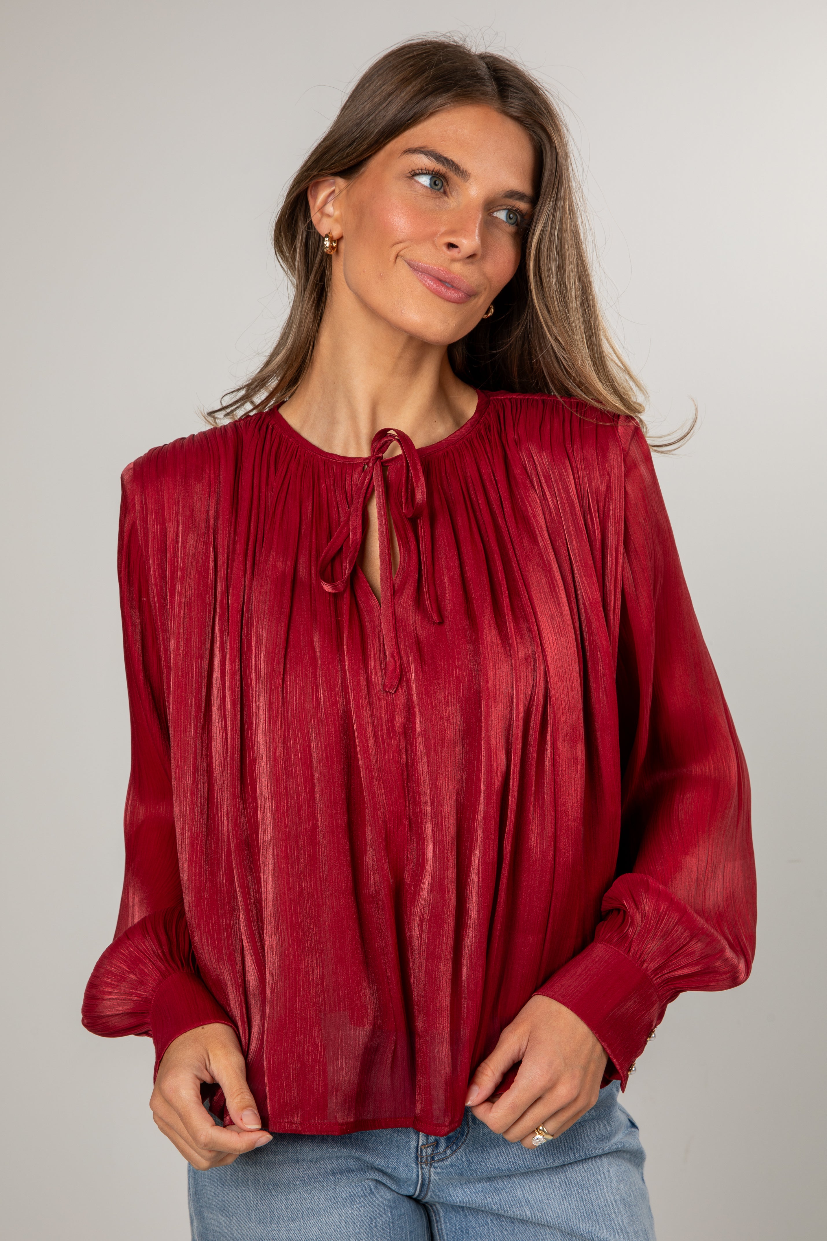 Woman wearing a red blouse with long sleeves against a plain background