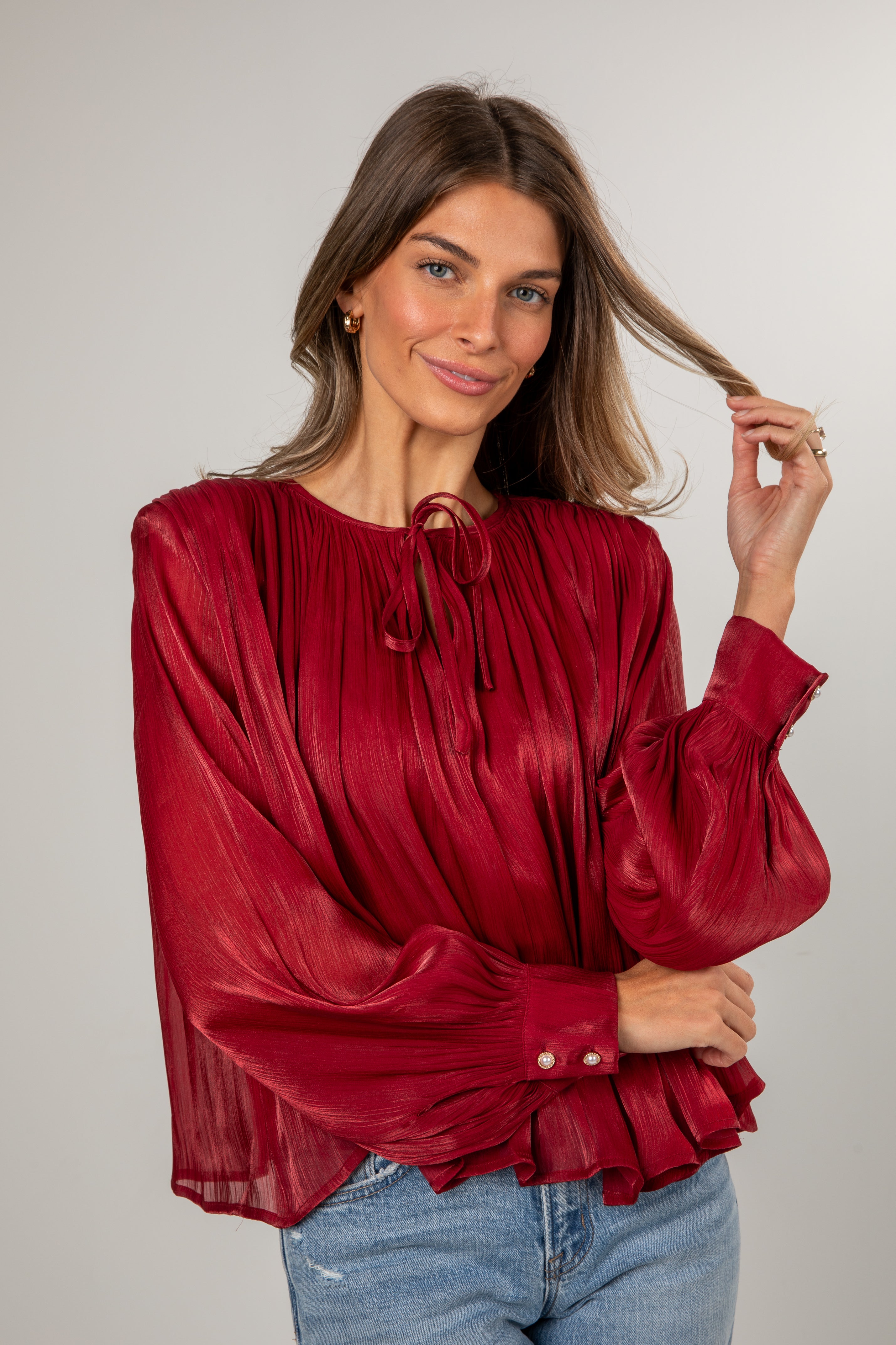 Woman wearing a red blouse with long sleeves and blue jeans on a plain background