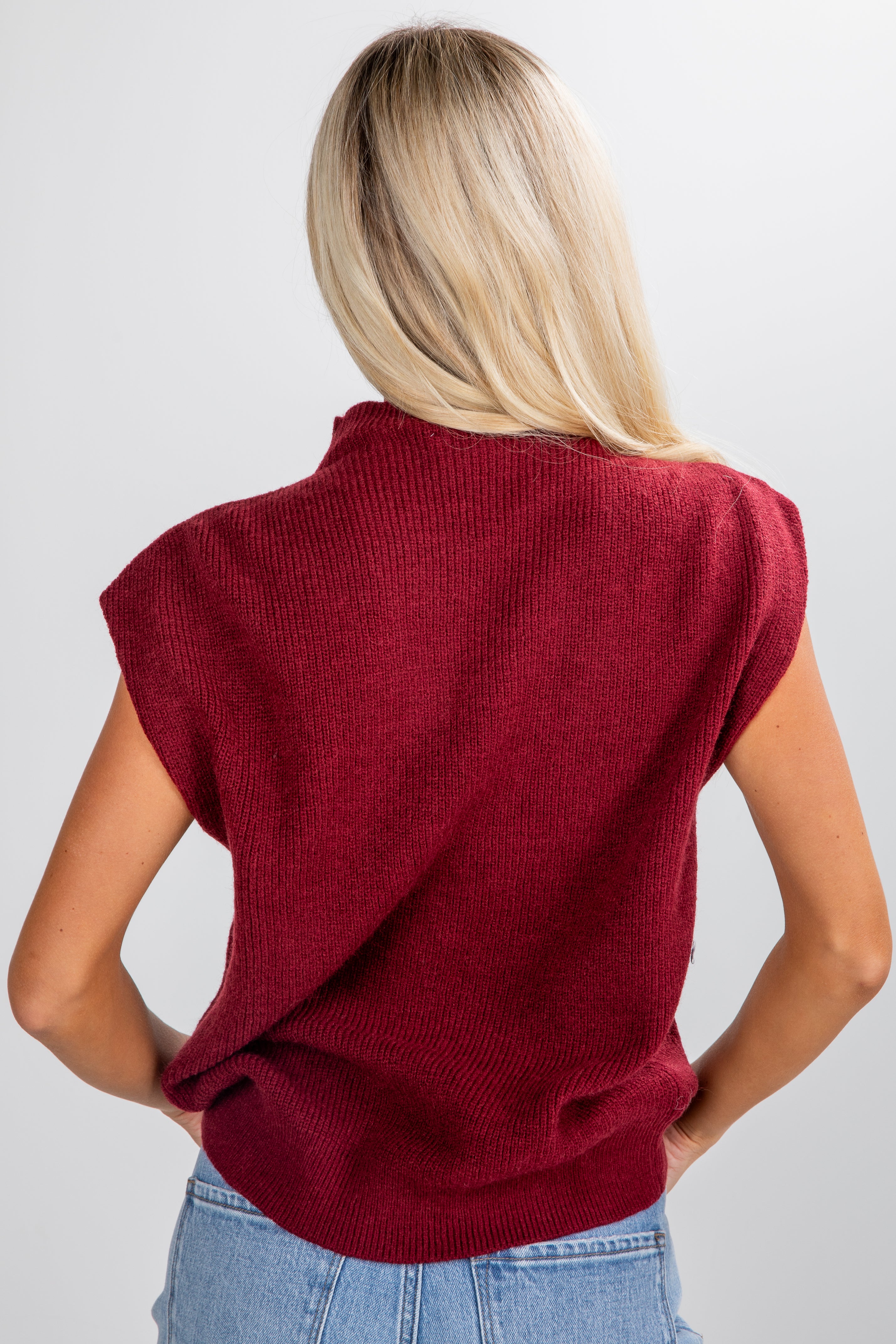 Person wearing a red sleeveless sweater against a white background