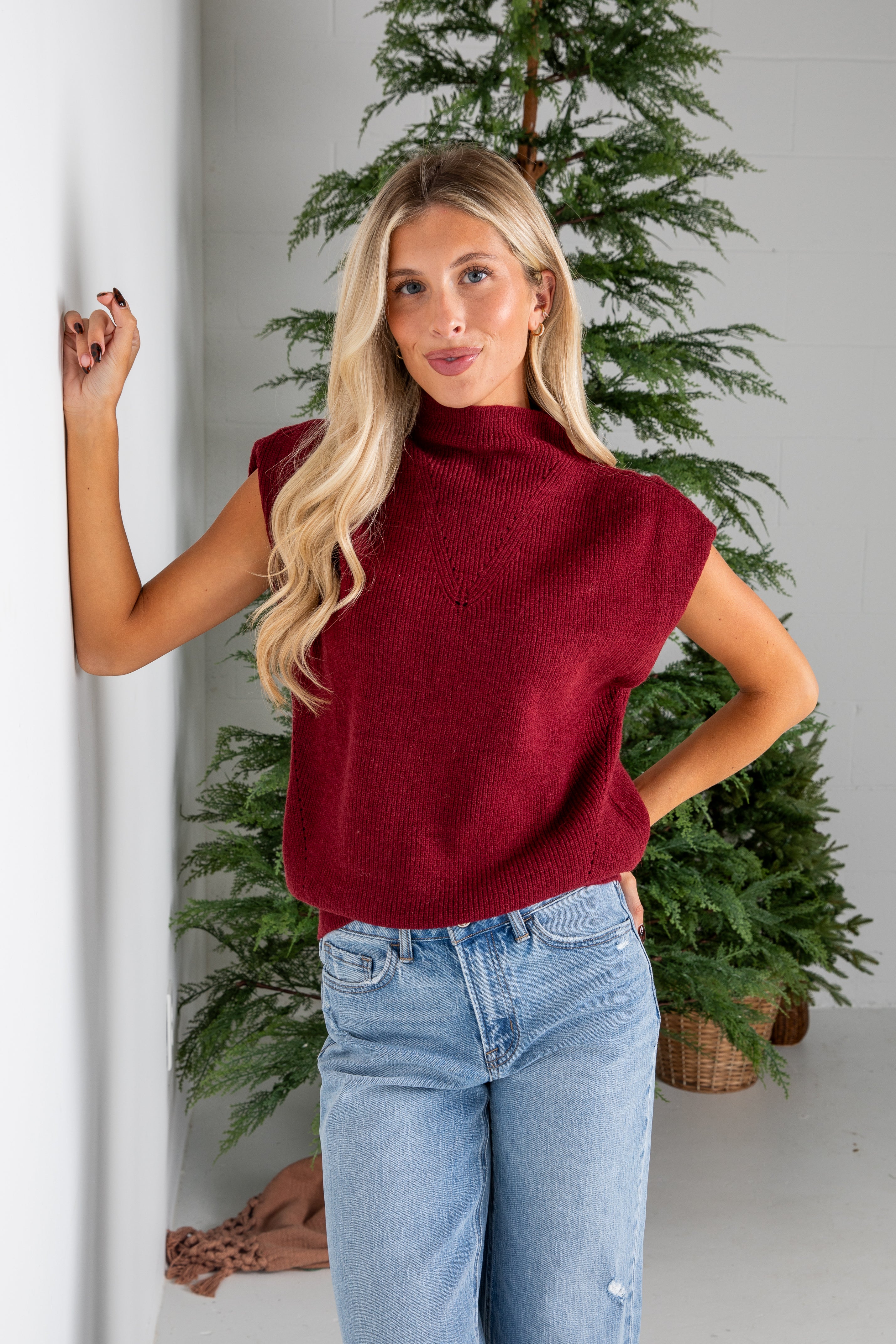 Woman wearing a red sweater and blue jeans standing in front of a Christmas tree.