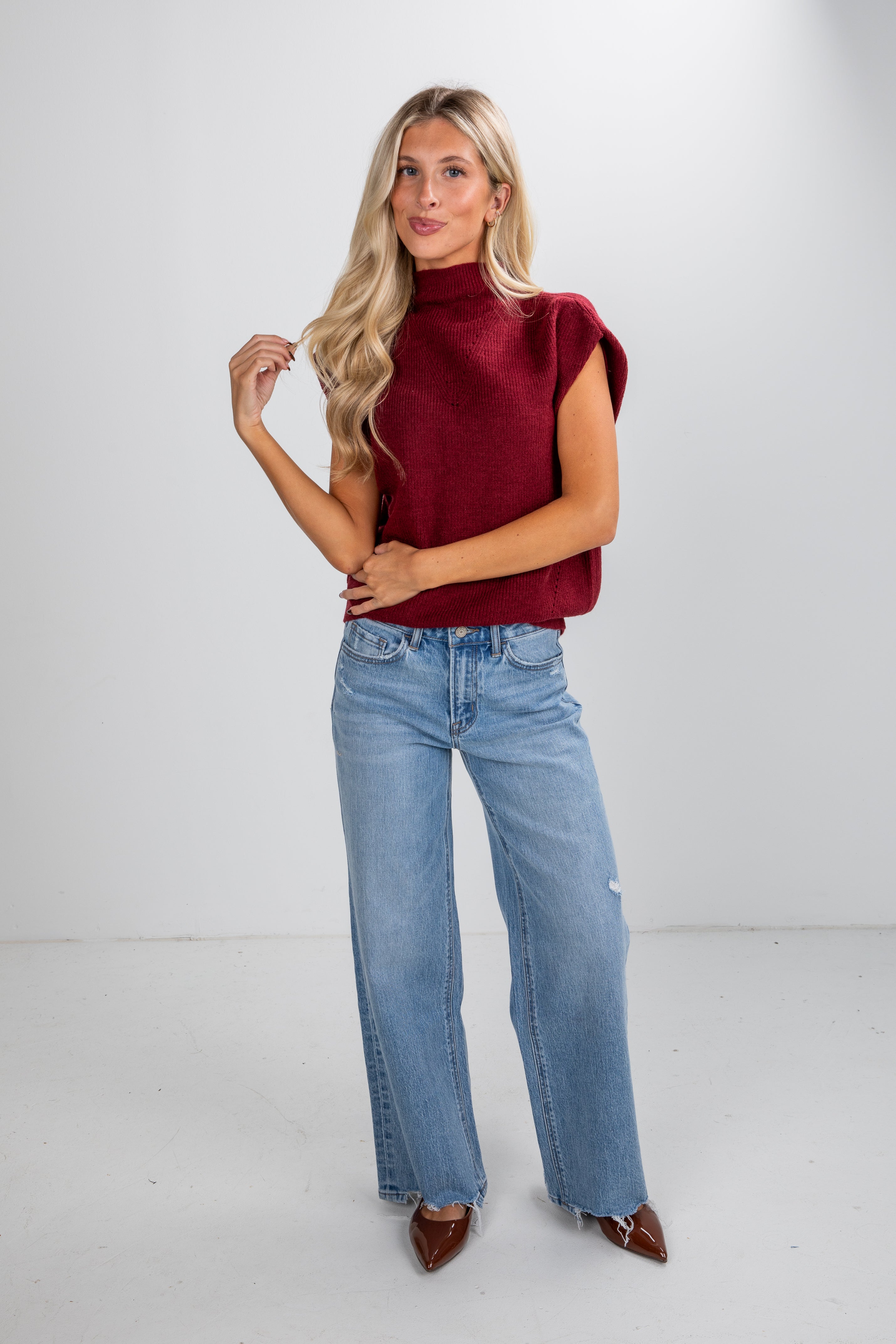 Woman wearing a red sleeveless sweater and blue jeans on a white background