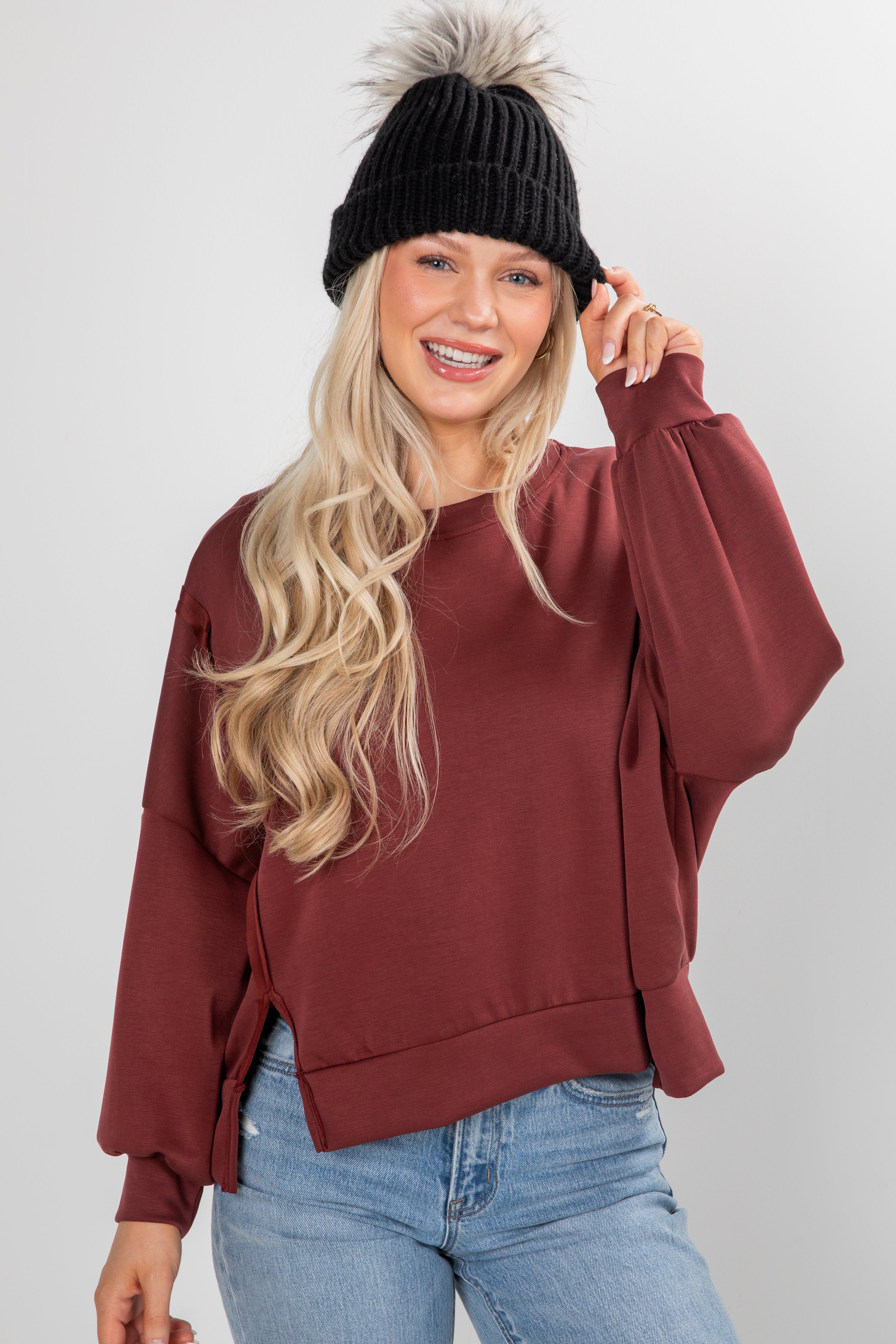 Woman wearing a maroon sweater, black beanie, and blue jeans on a white background