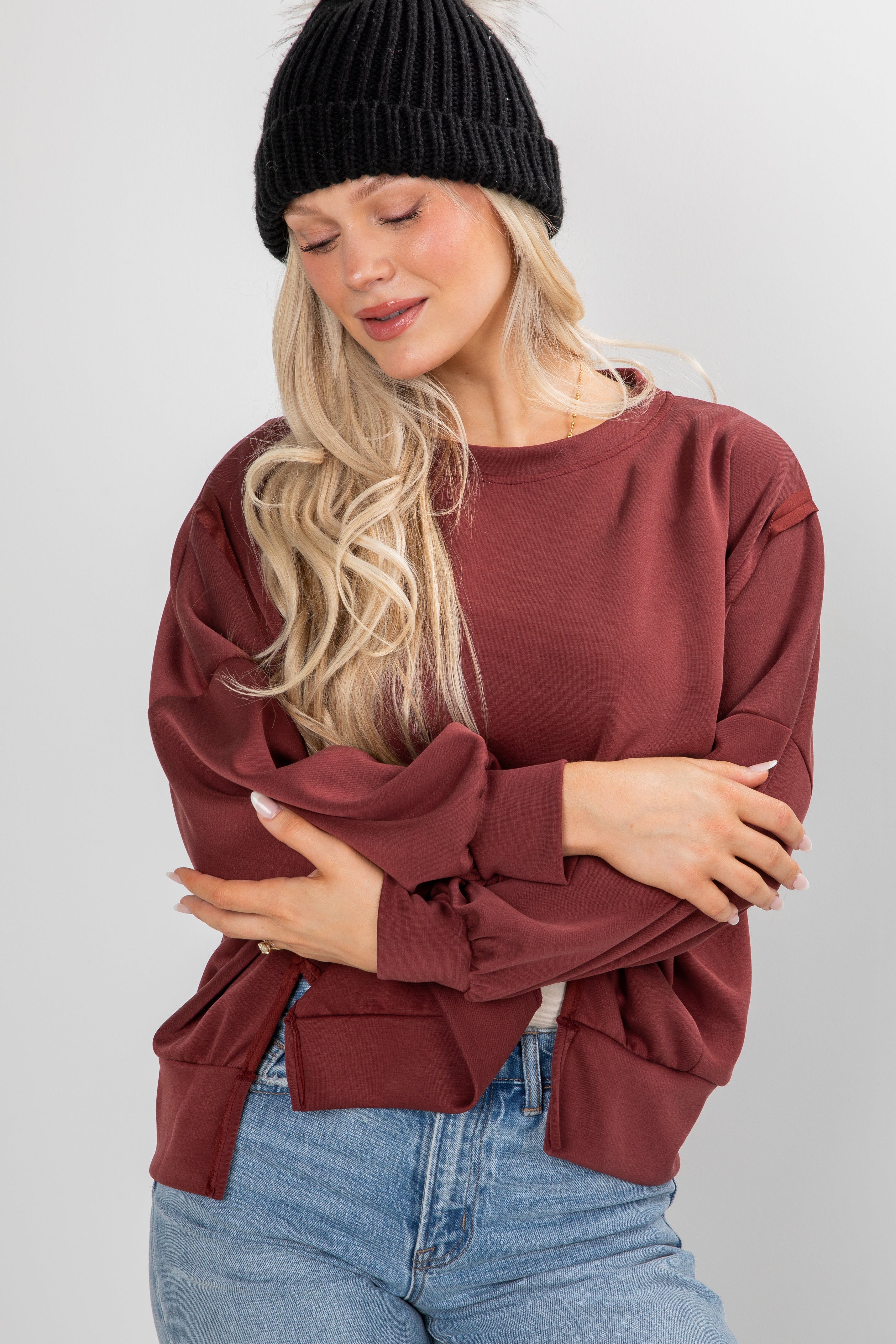 Woman wearing a burgundy sweater and black beanie against a plain background