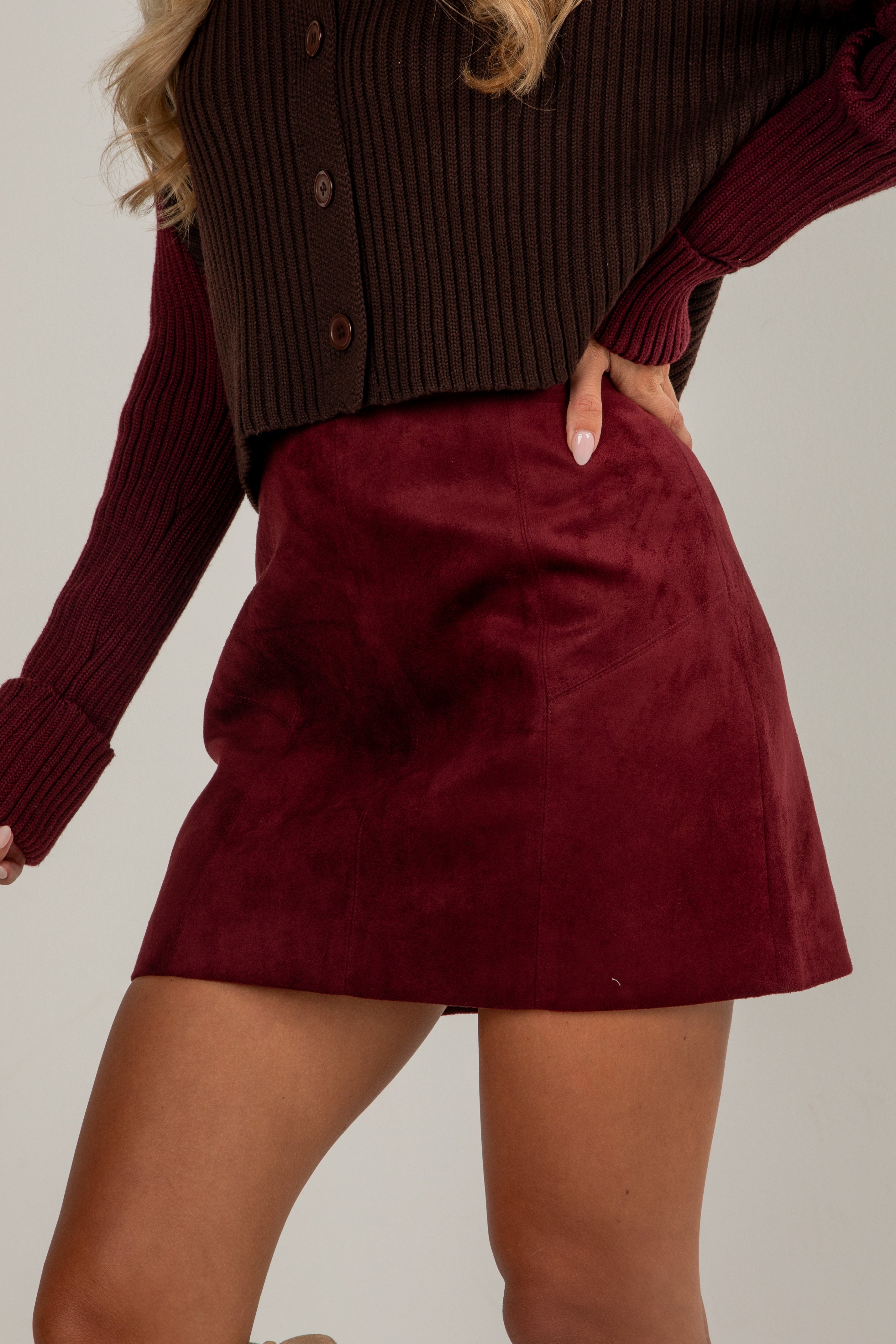 Person wearing a burgundy skirt and brown cardigan on a plain background