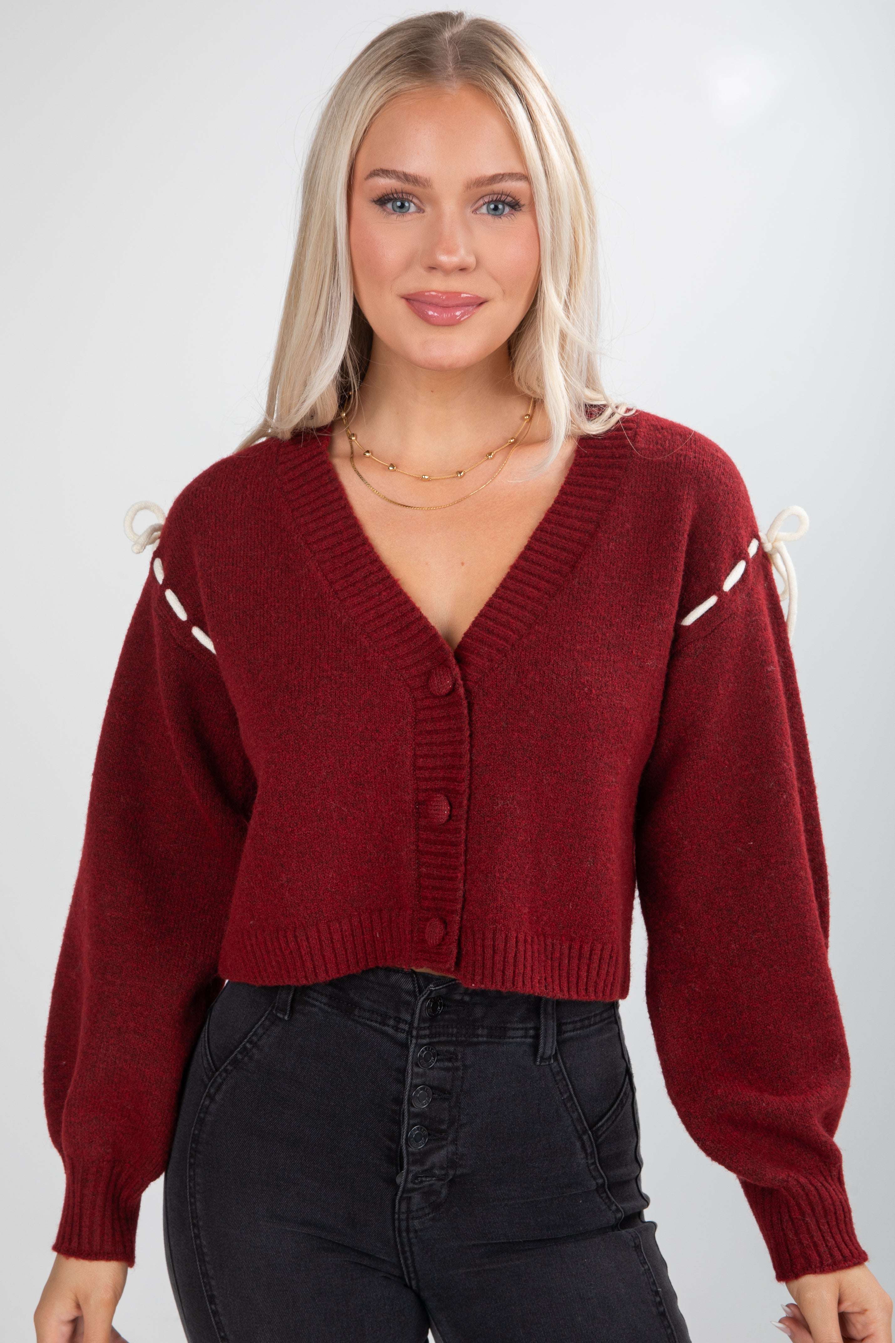 Woman wearing a red sweater with decorative buttons on a plain background