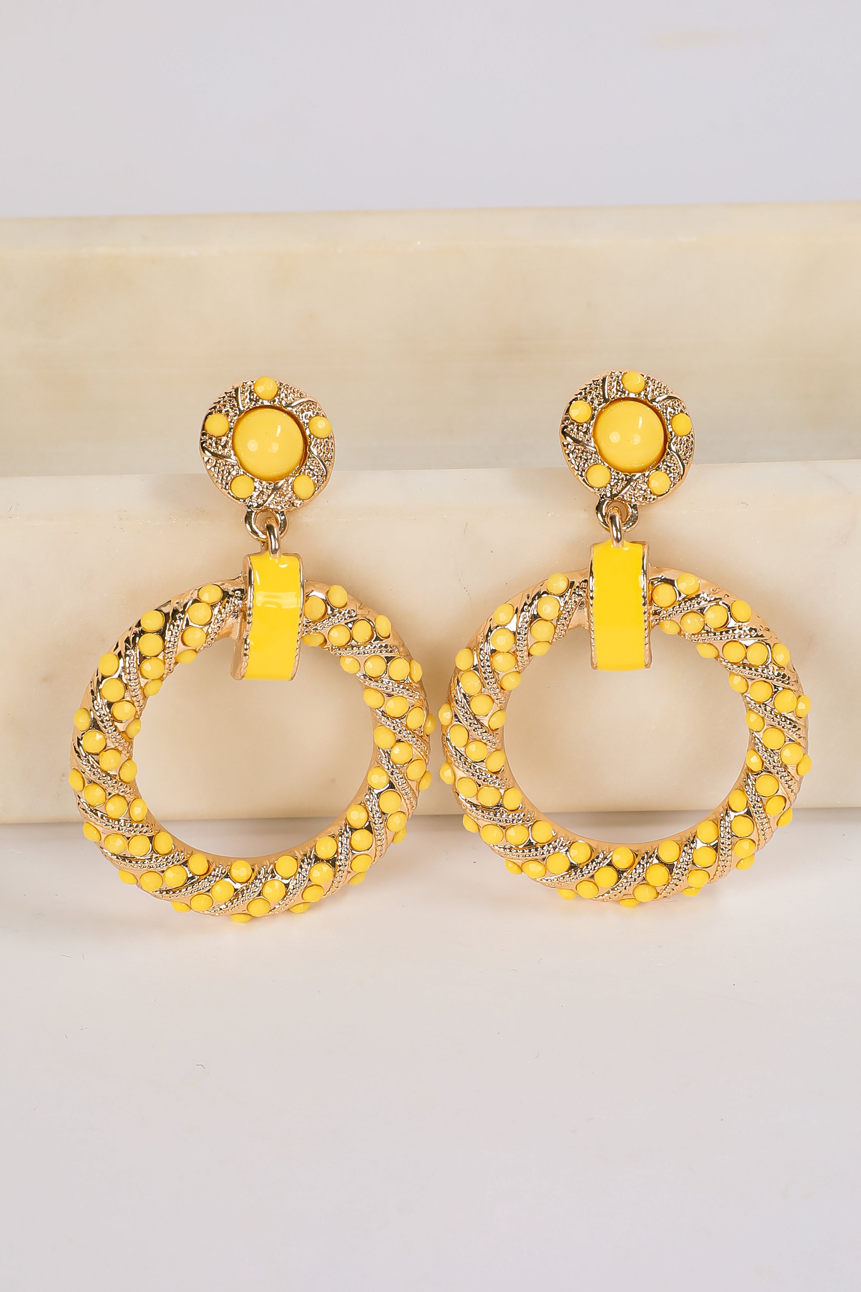 Pair of yellow hoop earrings with intricate designs on a light background
