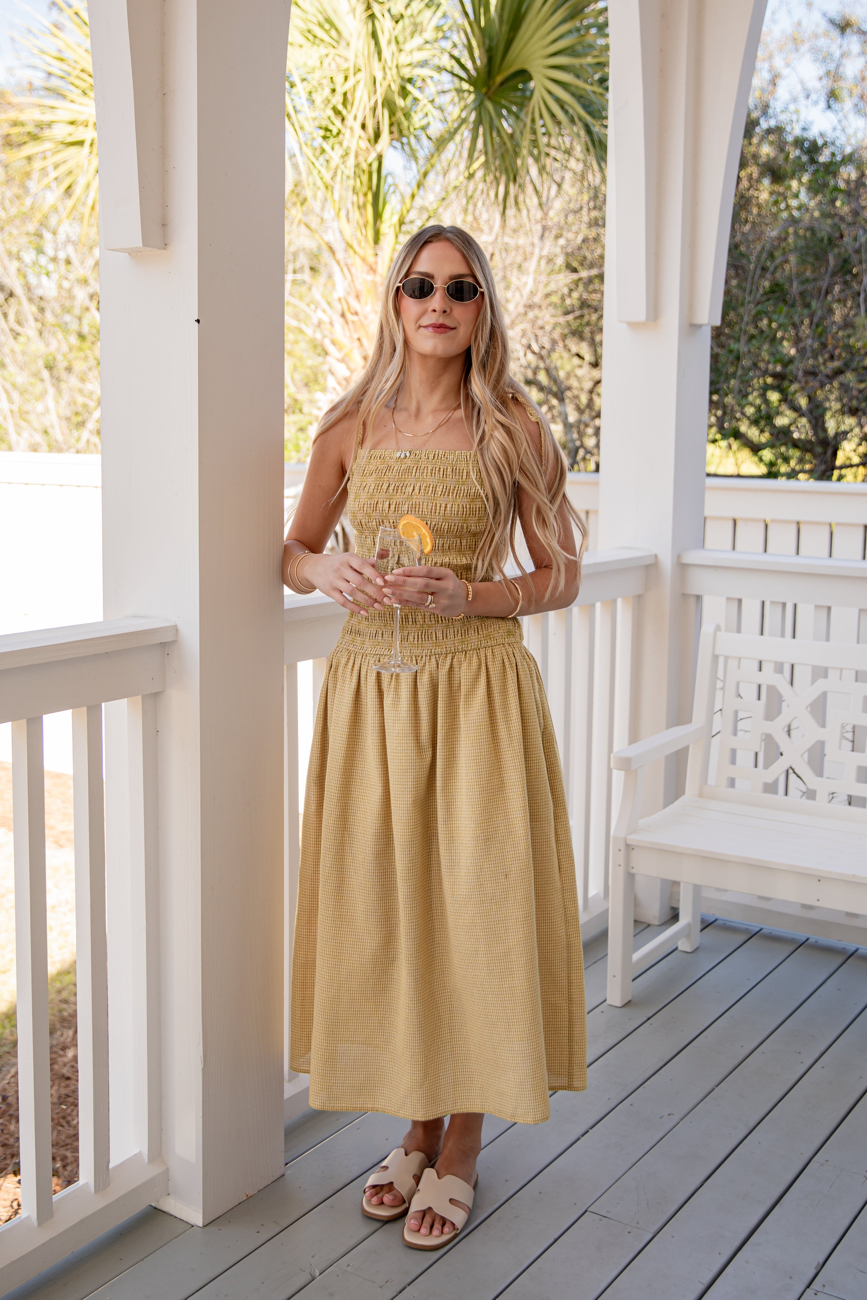 Woman in a yellow dress standing on a porch with greenery in the background