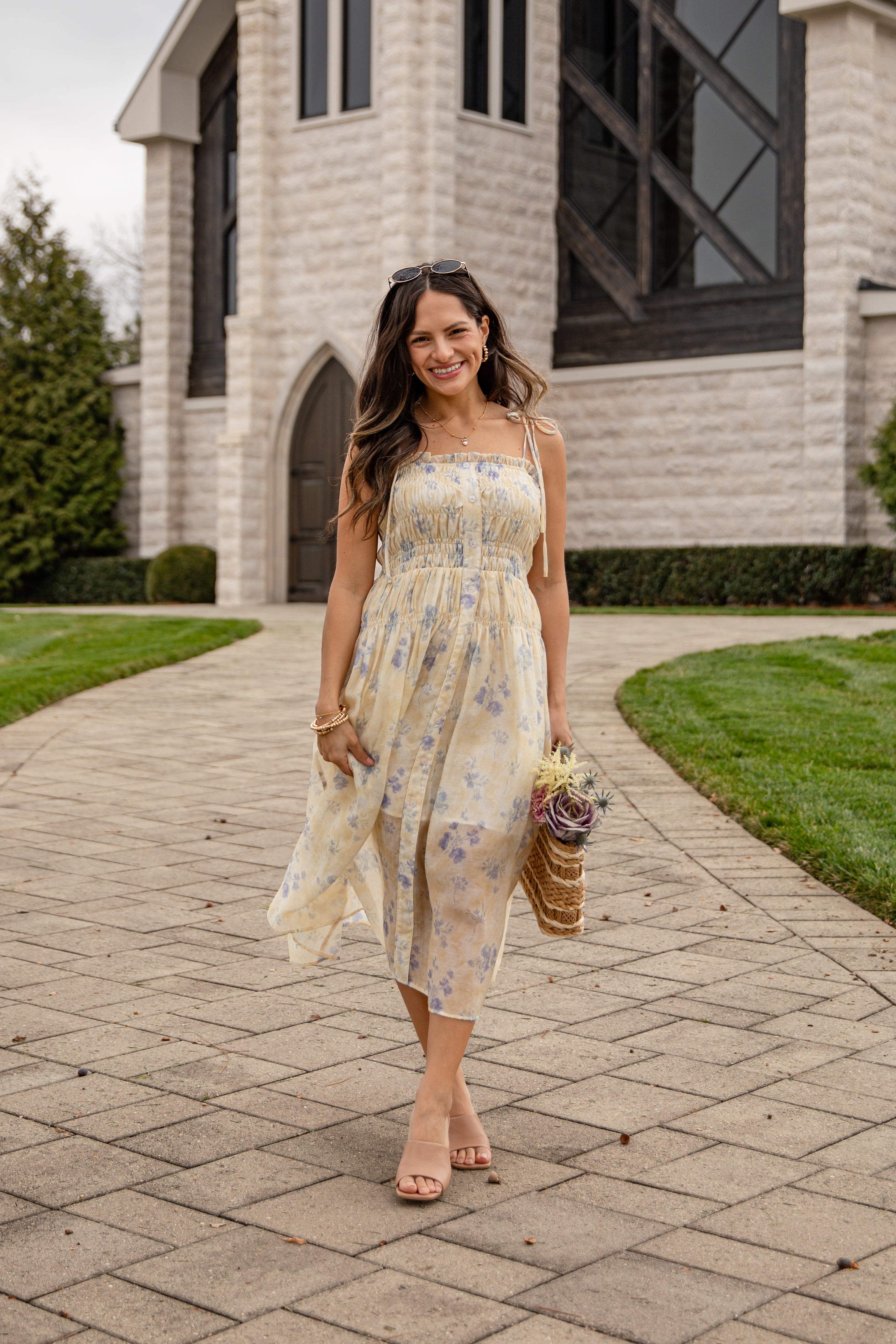 Woman in a floral dress standing on a paved walkway in front of a building.