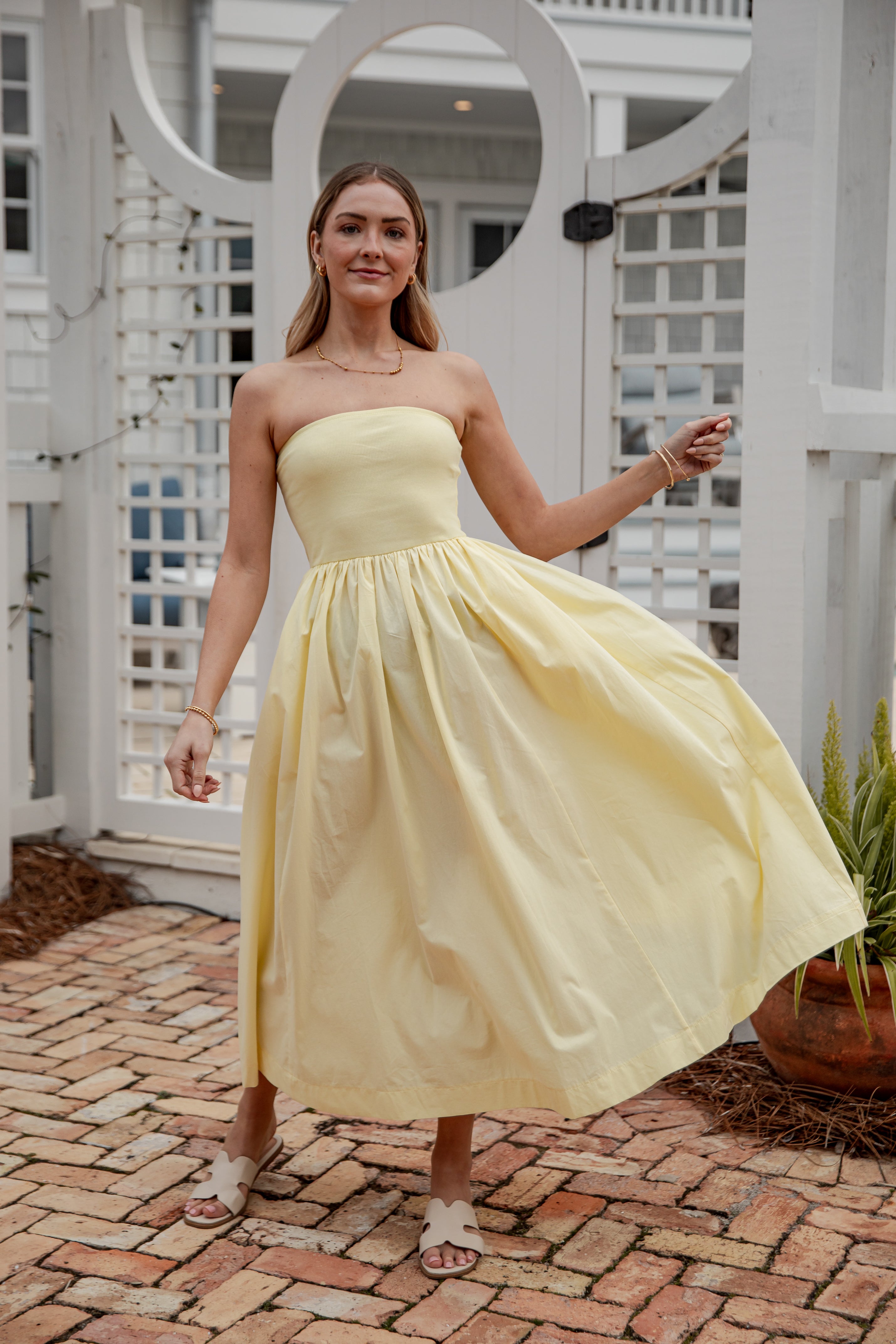 Woman in a yellow strapless dress standing outdoors on a brick path.