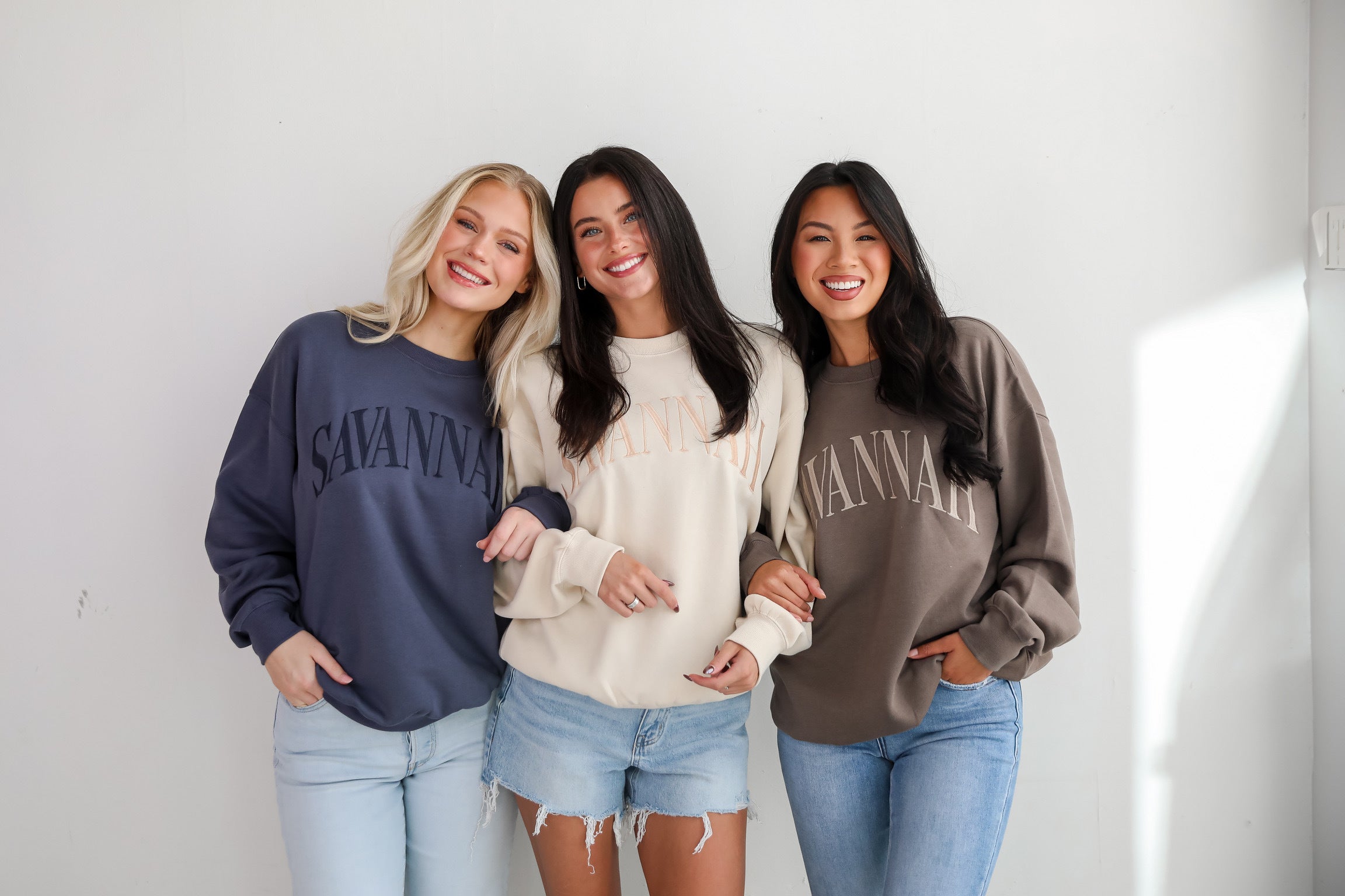 three models wearing embroidered sweatshirts