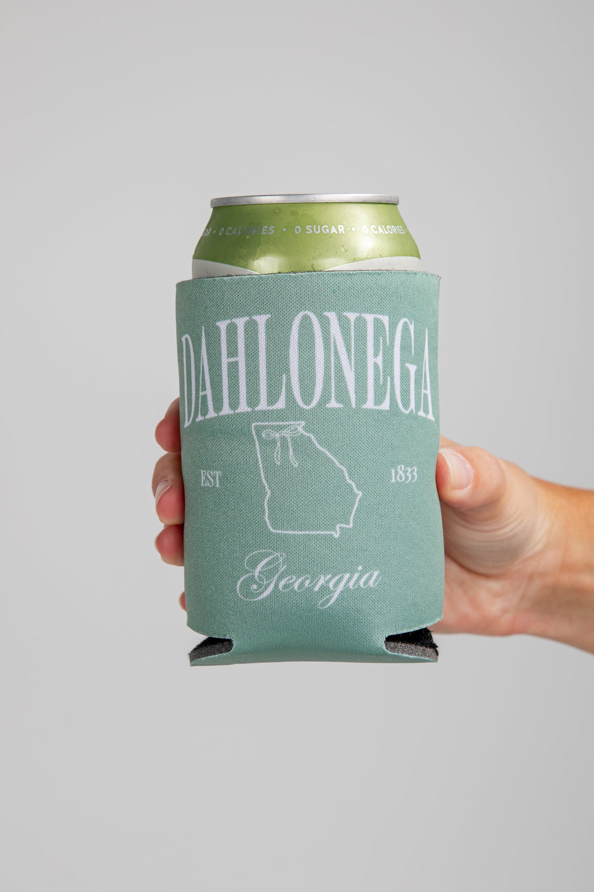 Hand holding a can with a green koozie labeled &
