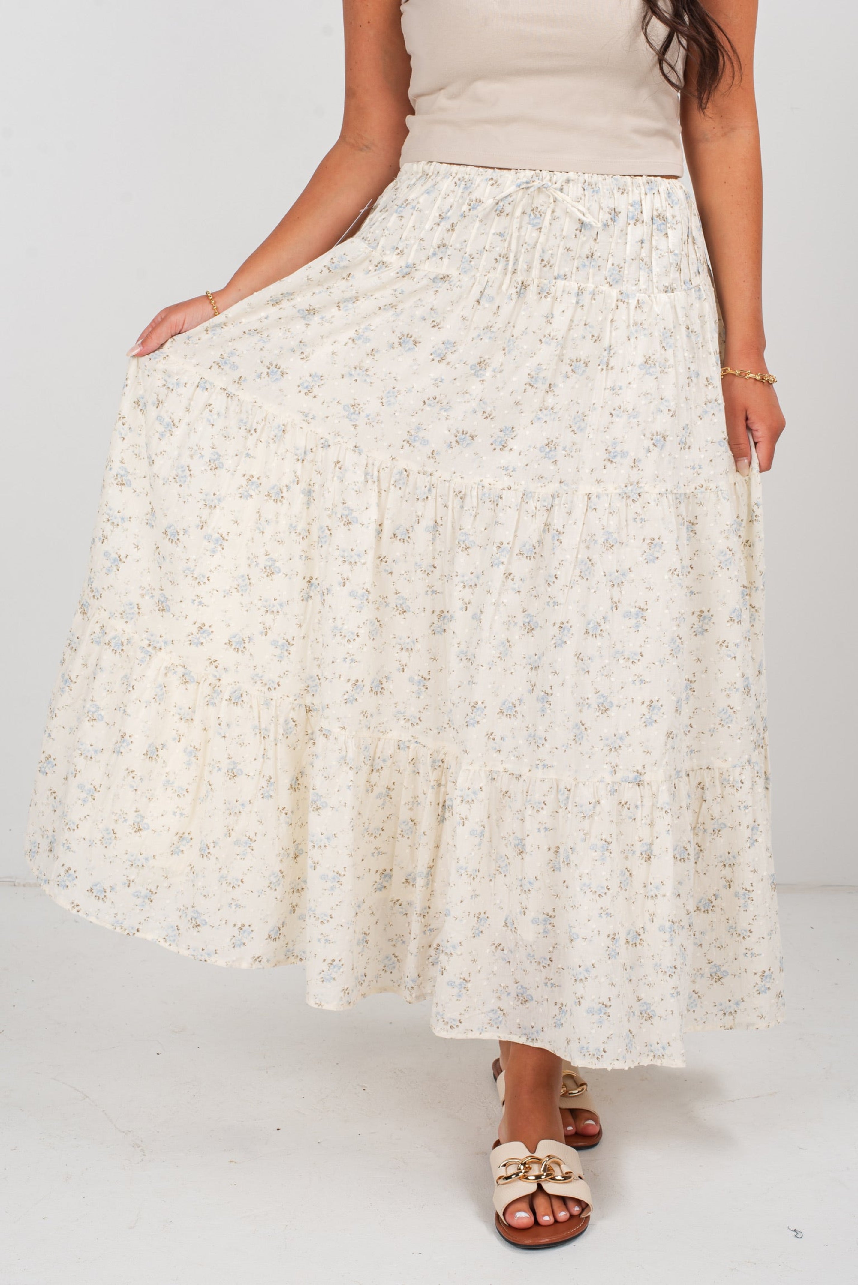 Woman wearing a long, light-colored floral skirt on a plain background