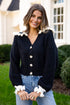 Woman wearing a navy blue cardigan with white trim in front of a house.