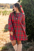 Woman wearing a red plaid dress with a bow in her hair, standing outdoors.