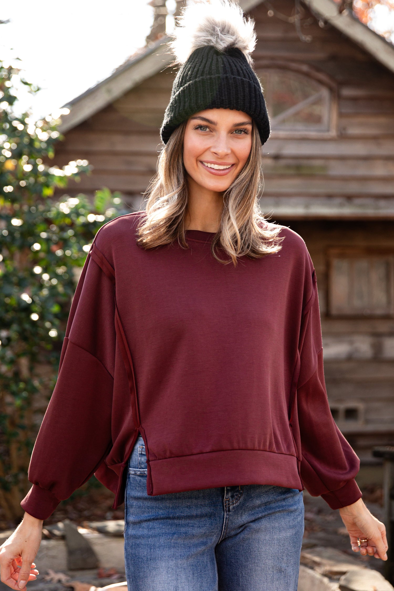 Woman wearing a burgundy sweater and black beanie standing in front of a wooden cabin.