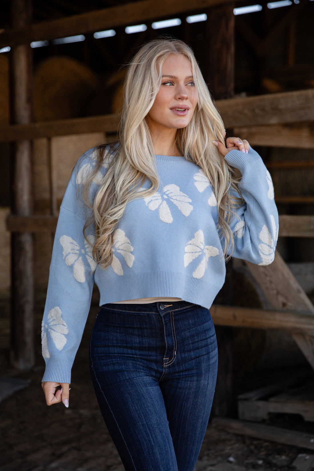 Woman wearing a light blue sweater with white floral patterns in a rustic setting.