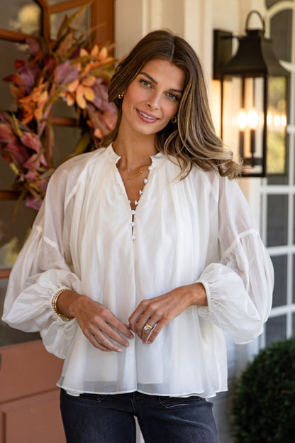 Woman wearing a white blouse standing in front of a door with decorative elements.