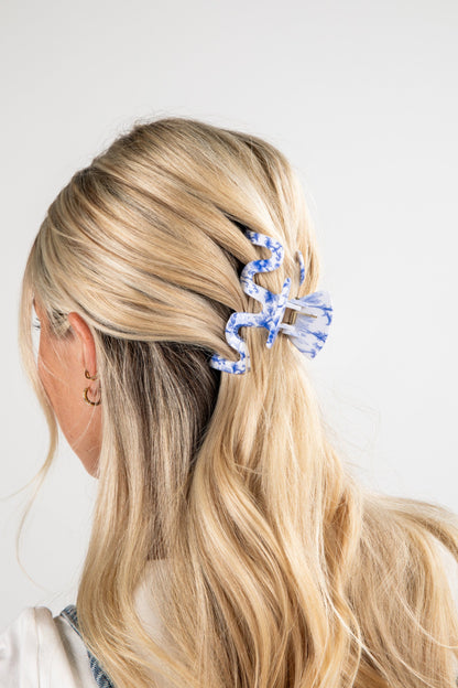 Person with blonde hair tied back using a blue hair clip on a white background
