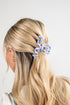 Person with blonde hair tied back using a blue hair clip on a white background