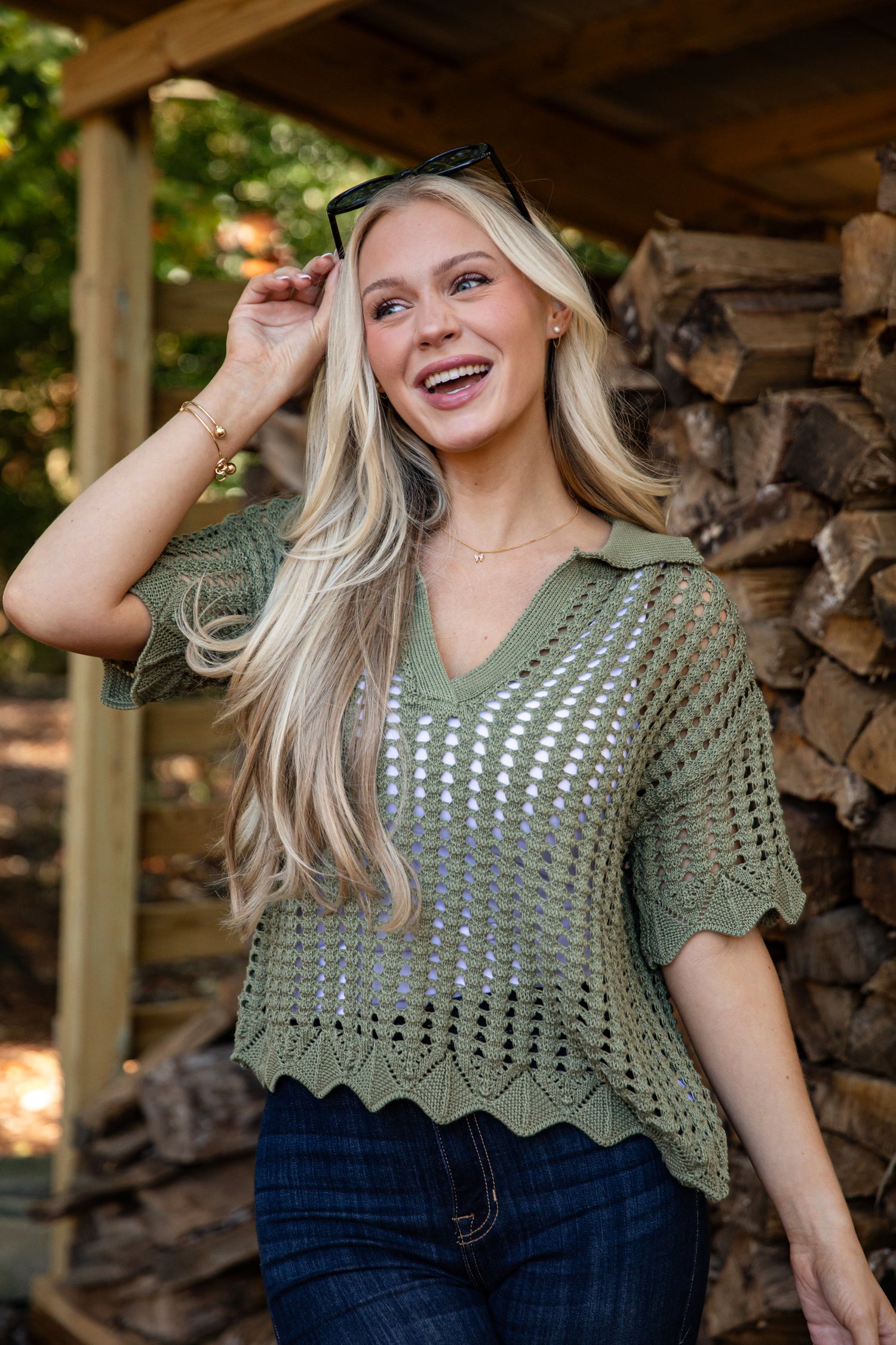 Woman wearing a green crochet top standing in front of stacked firewood.