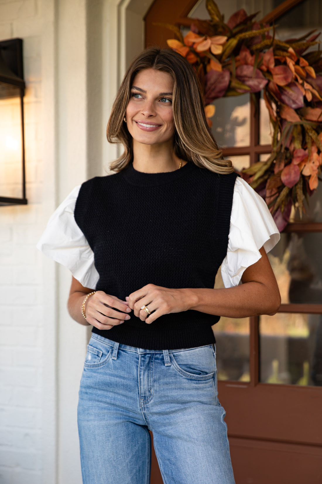 Woman wearing a black and white top with blue jeans standing indoors.