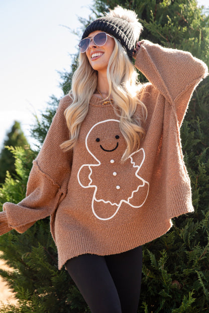 Person wearing a brown sweater with a gingerbread man design outdoors.