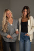 Two women wearing cardigans and jeans standing side by side against a plain background