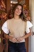 Woman wearing a beige knit vest over a white shirt with a blurred background