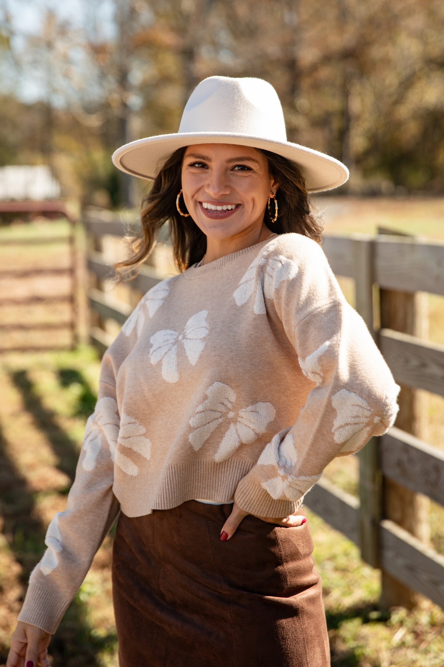 Woman wearing a beige sweater with butterfly patterns and a wide-brimmed hat outdoors.