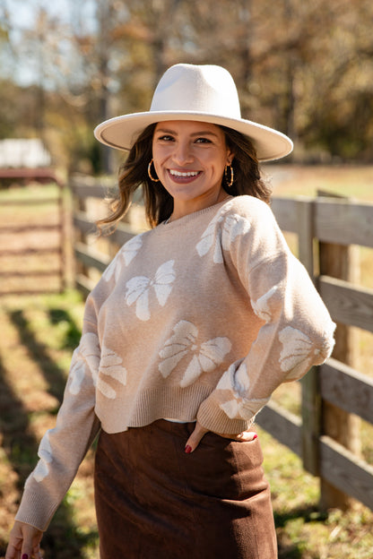 Woman wearing a beige sweater with butterfly patterns and a wide-brimmed hat outdoors.