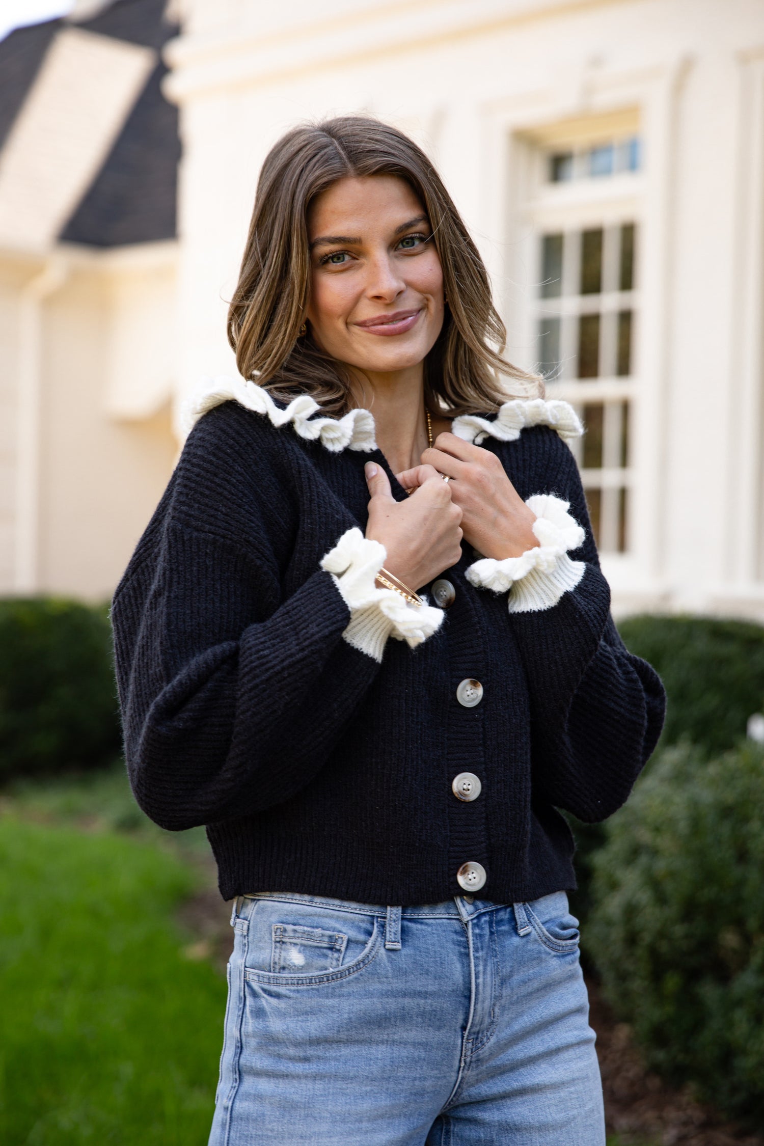 Woman wearing a black cardigan with white ruffled trim in front of a building.