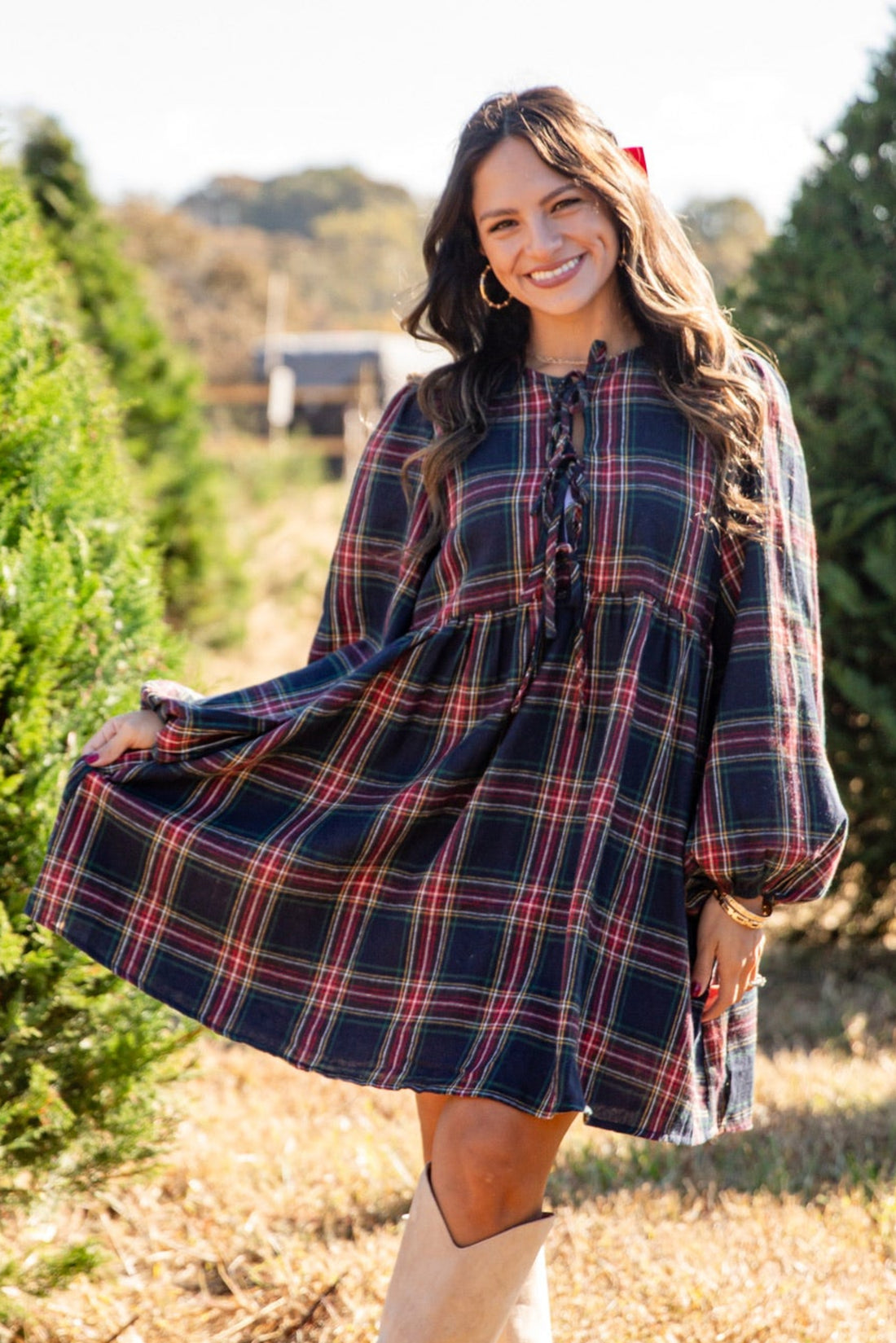 Woman in a plaid dress standing in a field with trees in the background