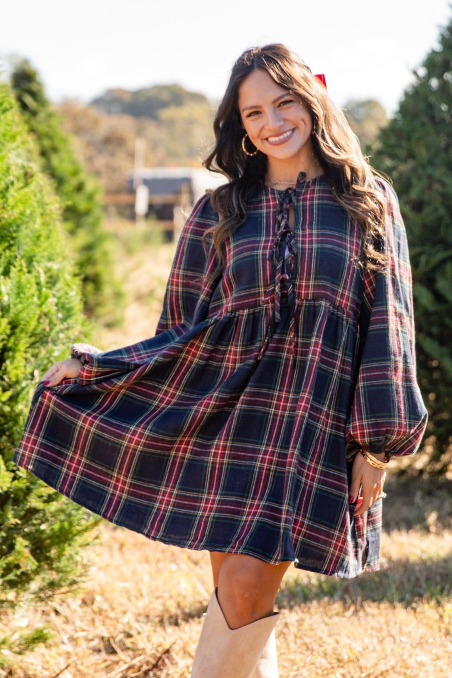 Woman in a plaid dress standing in a field with trees in the background