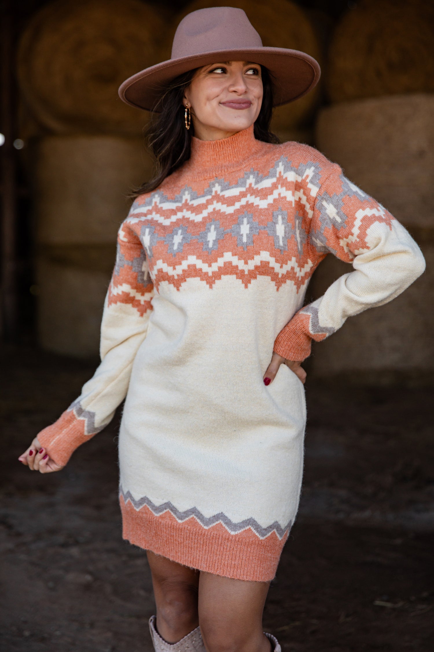 Woman wearing a patterned sweater dress and hat in a rustic setting
