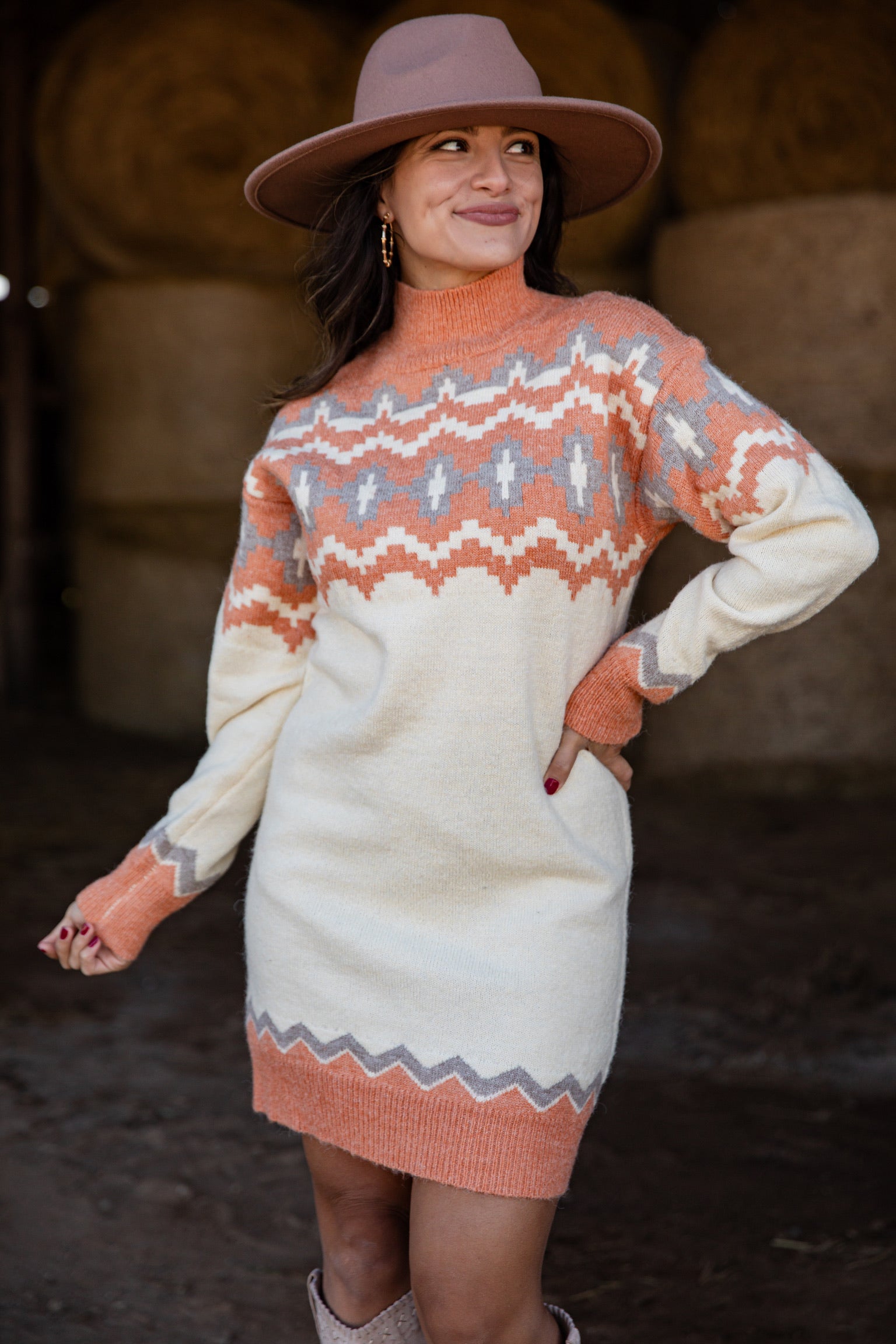 Woman wearing a patterned sweater dress and hat in a rustic setting