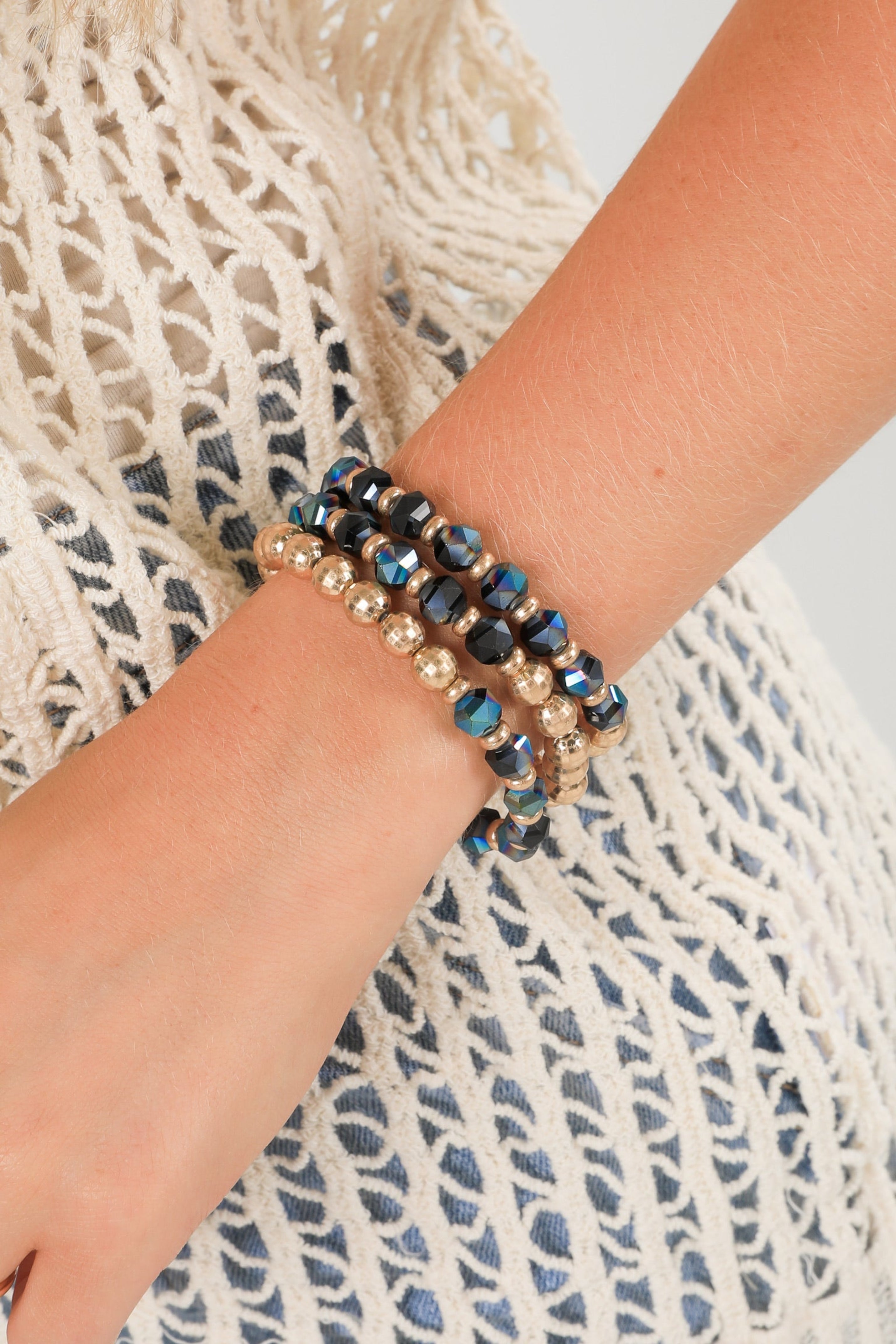 Three beaded bracelets on a wrist against a textured fabric background