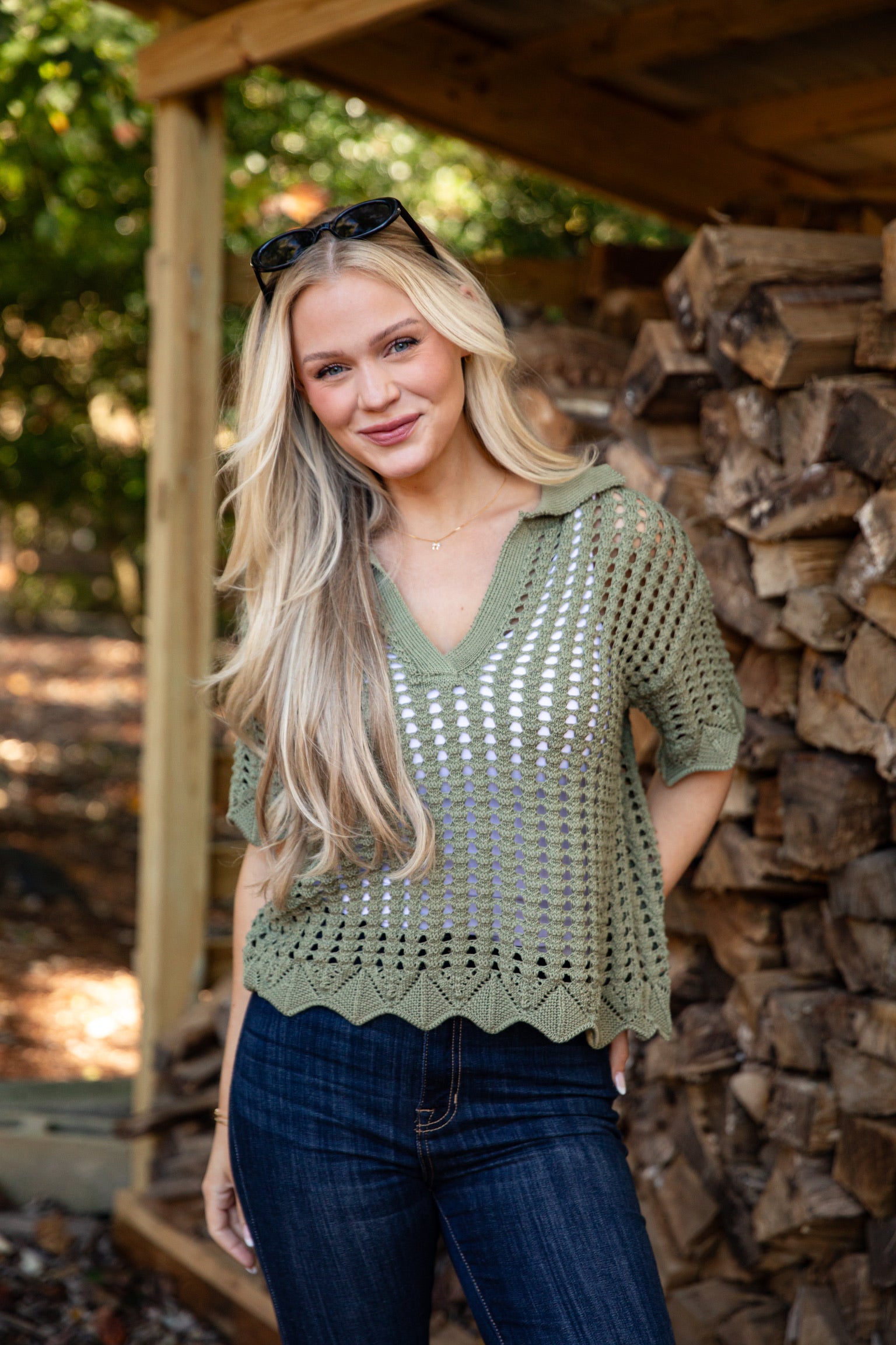Woman wearing a green crochet top standing in front of stacked wood.