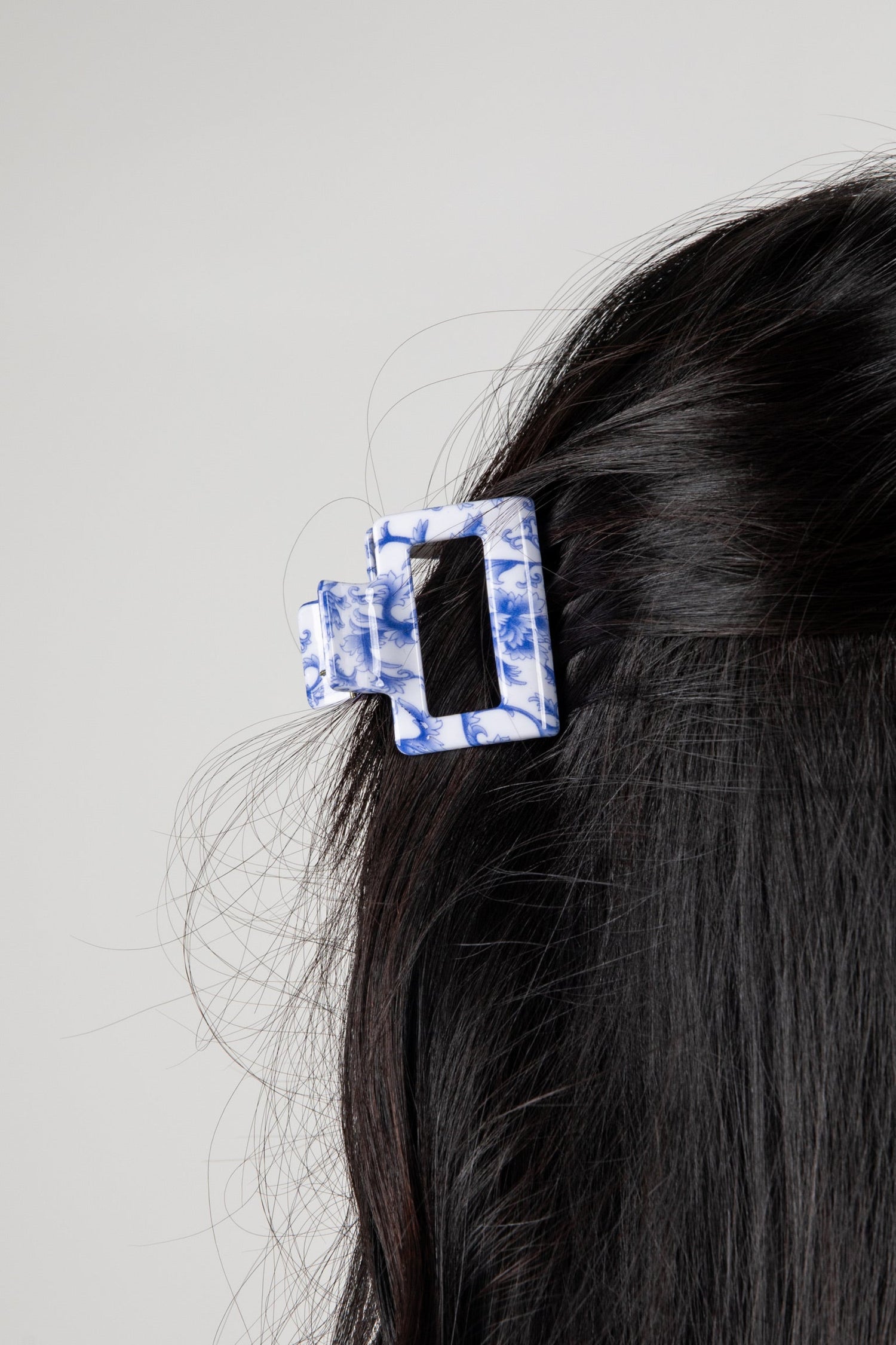 Hair clip with blue and white pattern on dark hair against a gray background