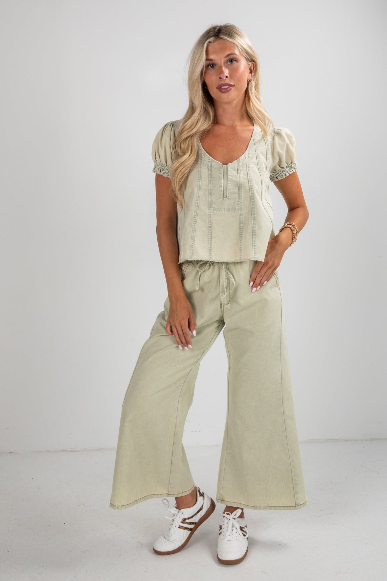 Woman wearing a light green outfit with wide-leg pants and a top against a white background