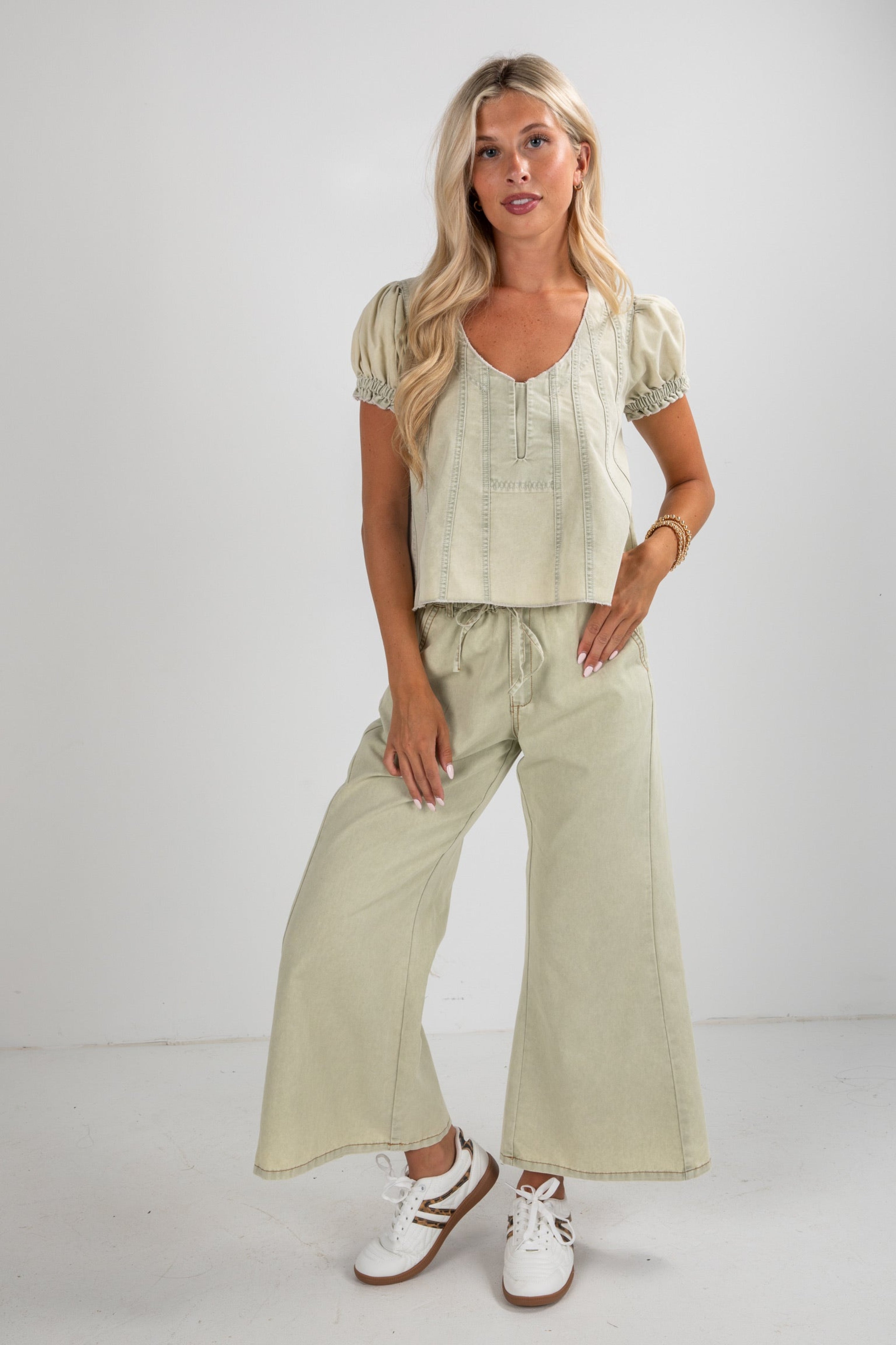 Woman wearing a light green outfit with wide-leg pants and a top against a white background