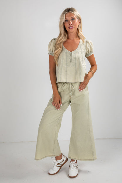 Woman wearing a light green outfit with wide-leg pants and a top against a white background