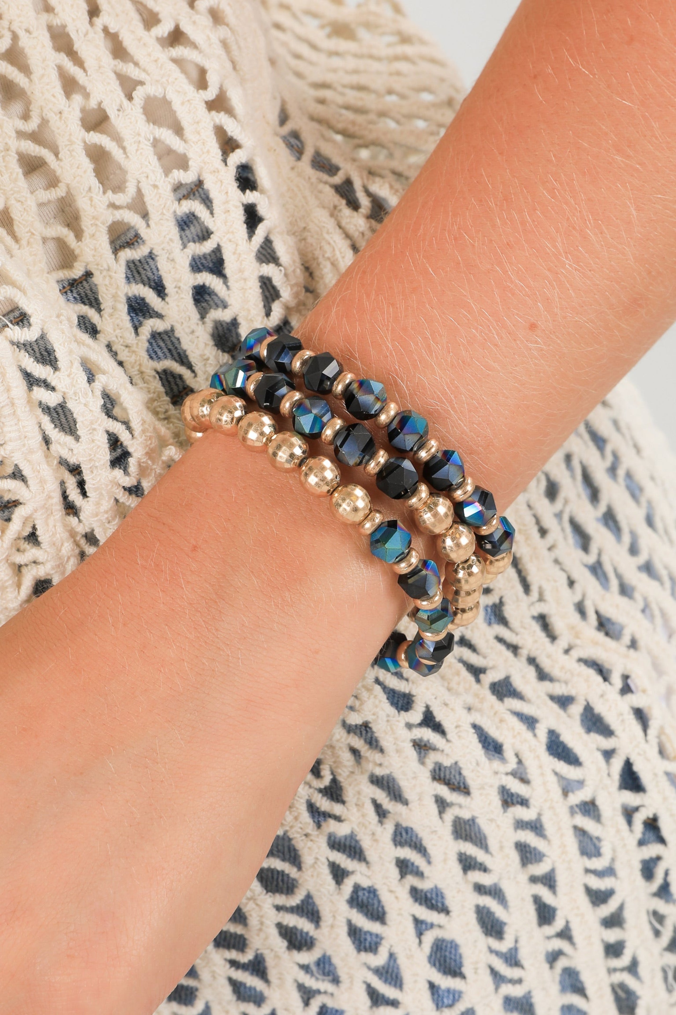 Close-up of a wrist wearing two beaded bracelets on a textured fabric background