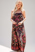 A woman modeling a sleeveless maxi dress with a black base and a vibrant, multicolored paisley and floral pattern in pink, red, orange, and green, set against a plain light gray background.