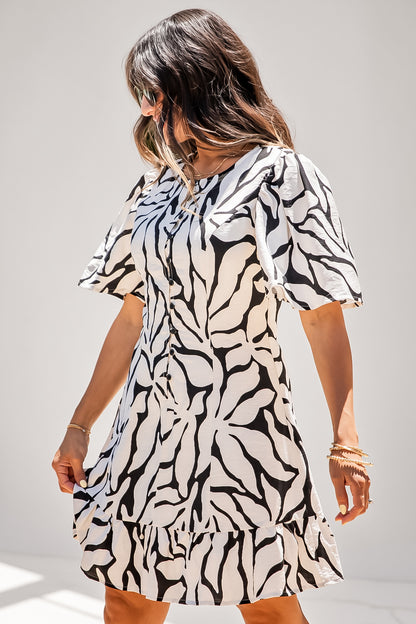 A woman wearing a short-sleeve dress with a bold black and off-white abstract leaf pattern, photographed against a plain light gray studio background.