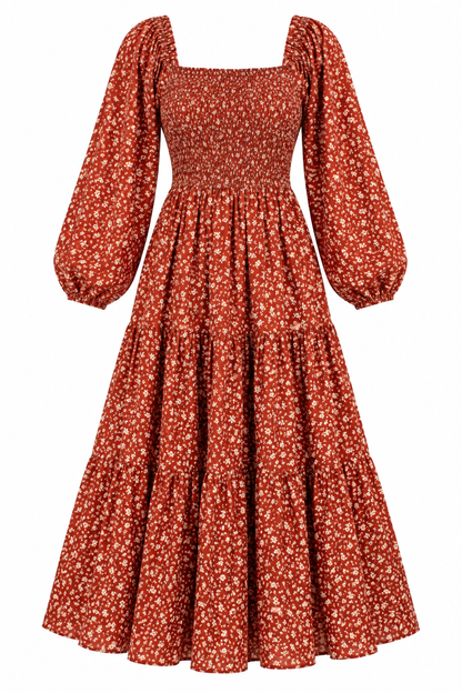 A long-sleeved midi dress with a smocked bodice and tiered skirt, featuring a rust red and white floral pattern, shown against a plain white background.