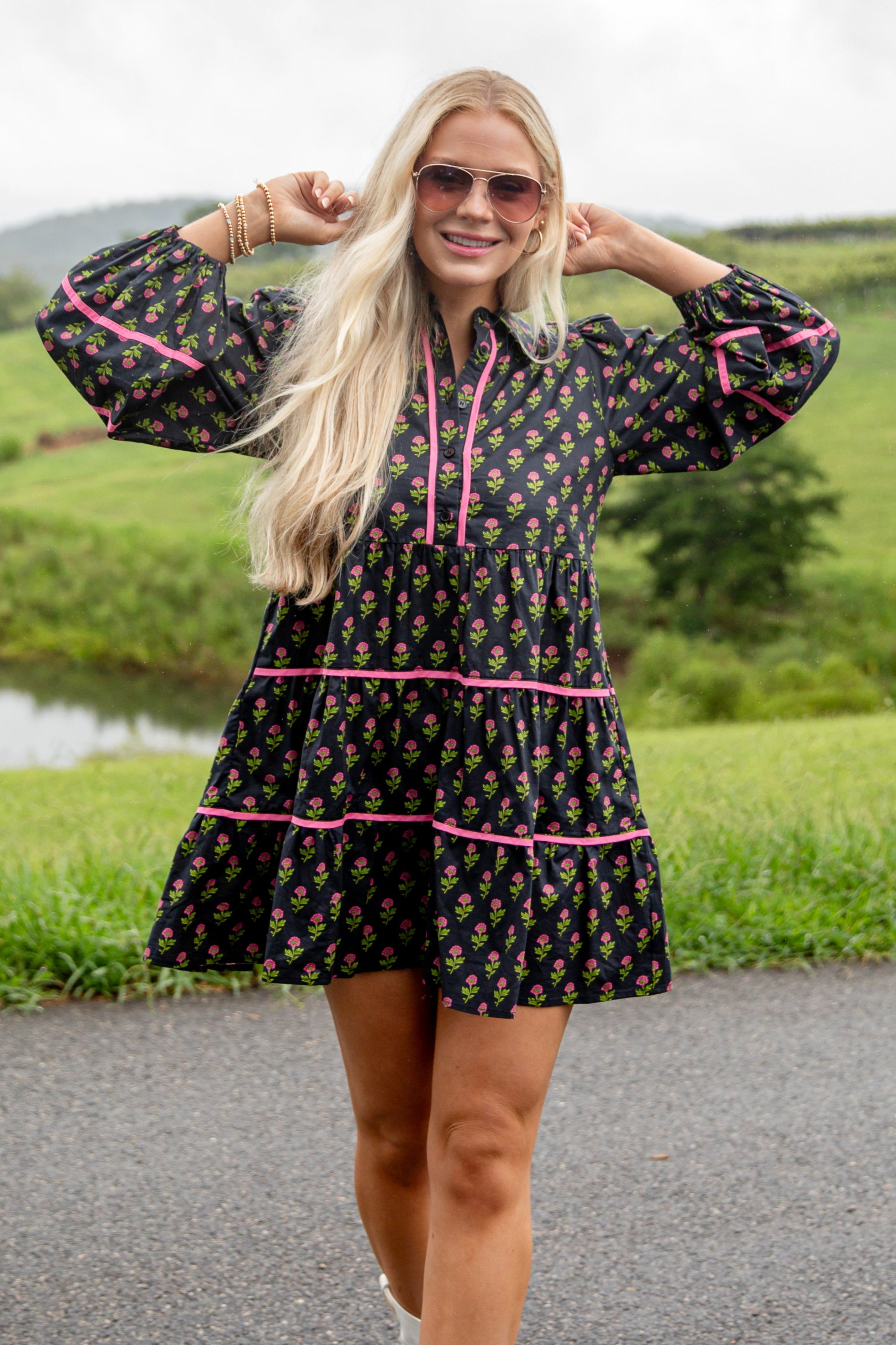 Woman in a patterned dress with pink accents standing on a road with greenery in the background