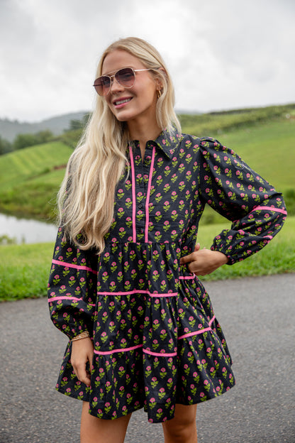 Woman wearing a floral dress with pink accents standing outdoors with green hills in the background