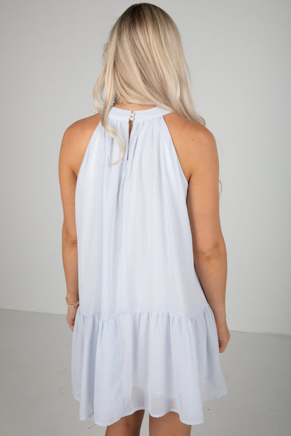 Woman wearing a white dress with a halter neck and ruffled hem on a plain background